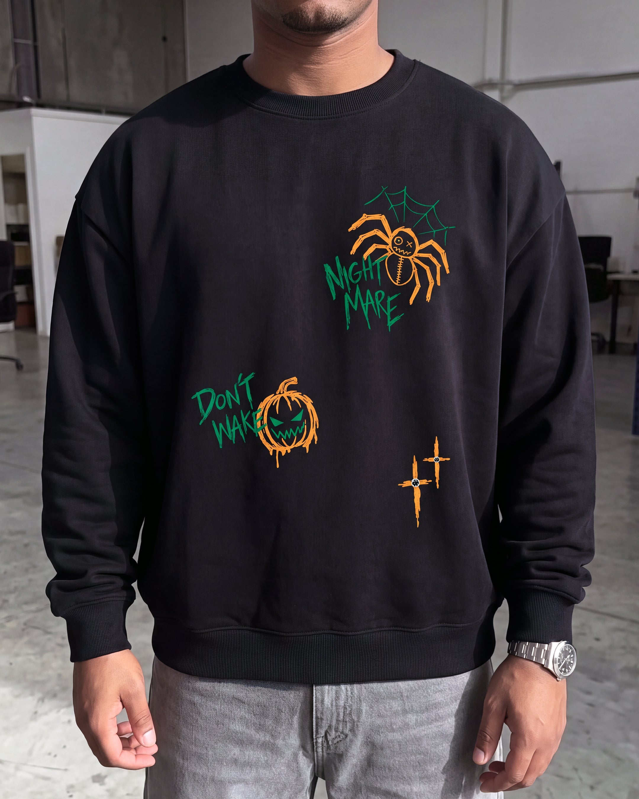 A man wearing a black crewneck sweatshirt with Halloween-themed graphic prints, including a spider, a pumpkin, and the text 'Mighty Mare' and 'Don't Worry'.