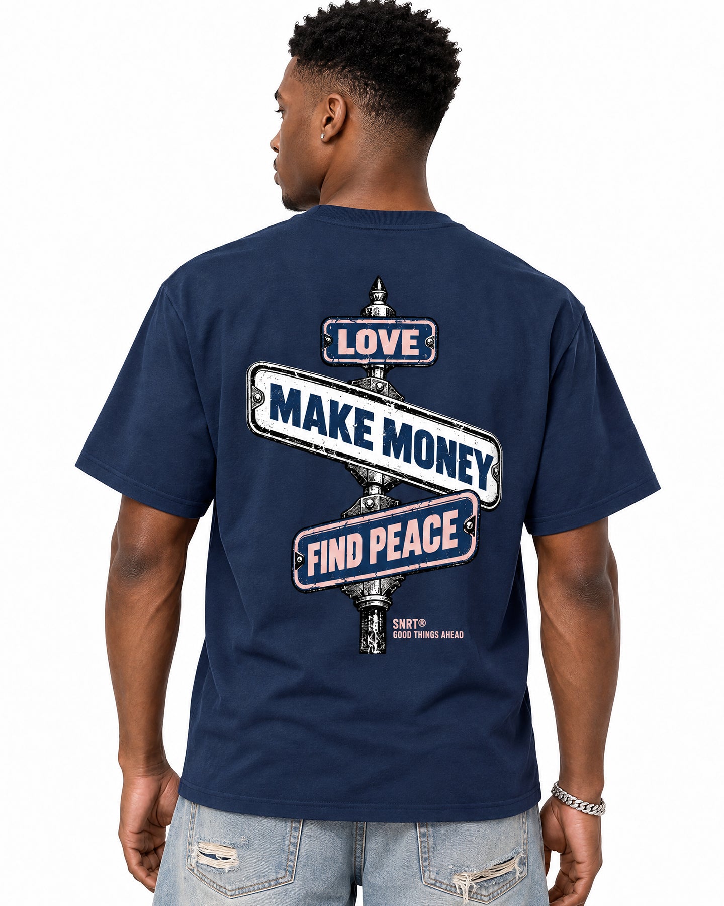A man wearing a navy blue t-shirt with a graphic on the back, shown from behind. The graphic features three signpost directions with the words 'LOVE', 'MAKE MONEY', and 'FIND PEACE' in white and red.