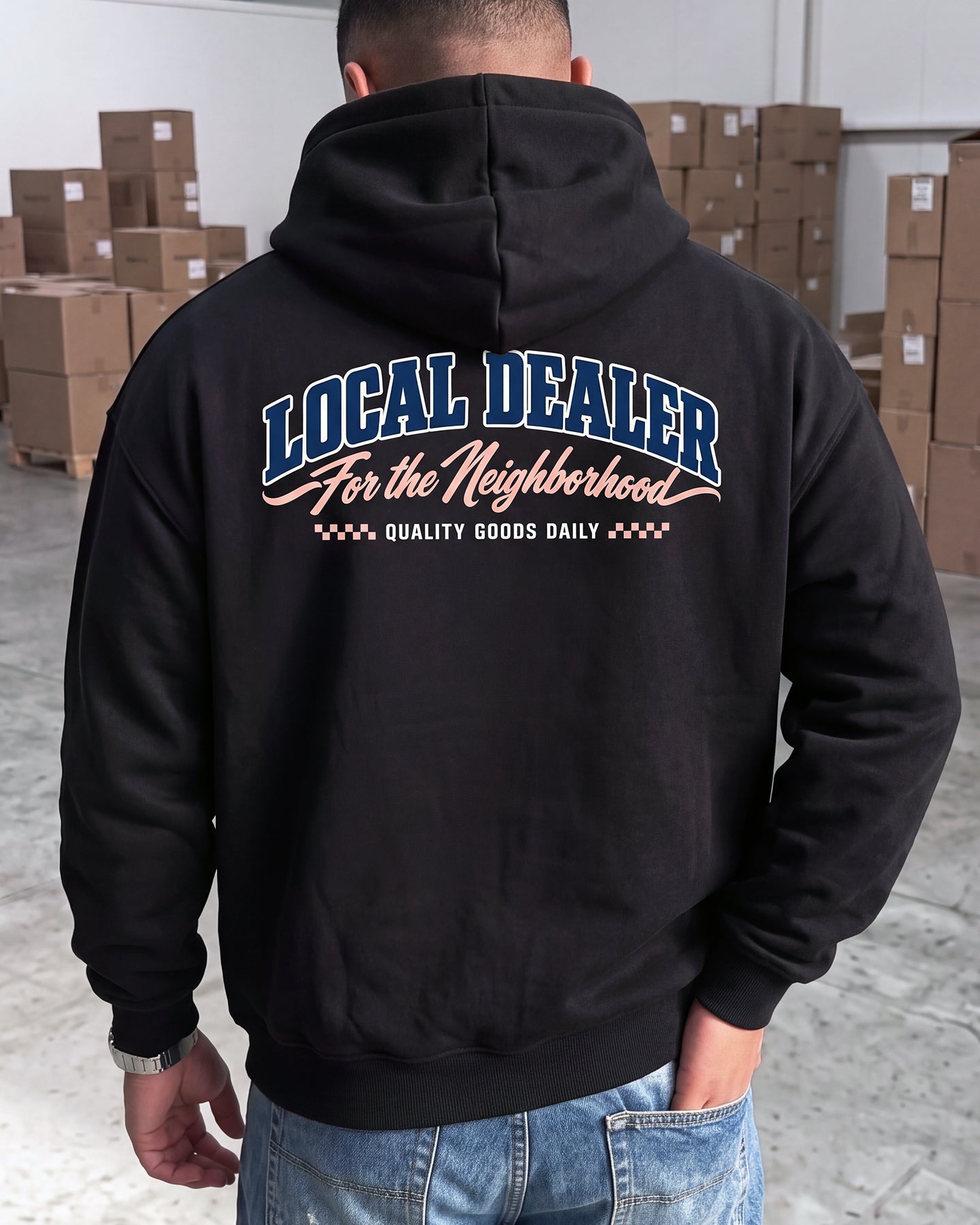 A man viewed from behind wearing a black pullover hoodie with a large graphic on the back. The graphic reads 'LOCAL DEALER For the Neighborhood' in blue and white, with 'QUALITY GOODS DAILY' below in white.