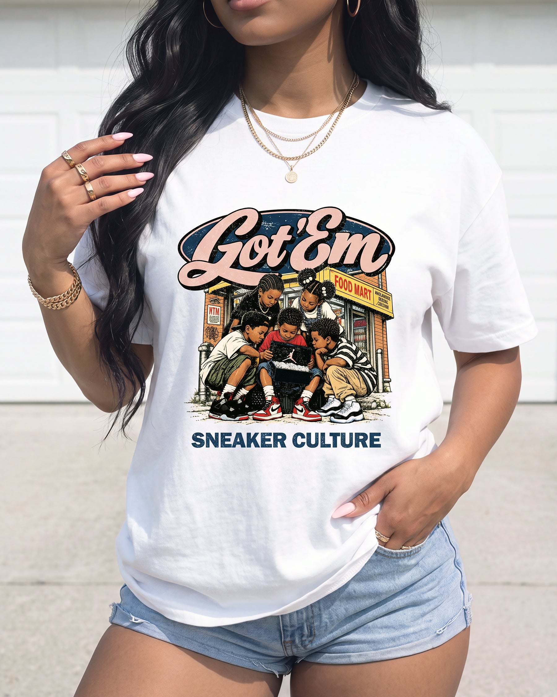 A woman wearing a white graphic t-shirt with a 'Got 'Em Sneaker Culture' print, paired with denim shorts, set against a neutral outdoor background.