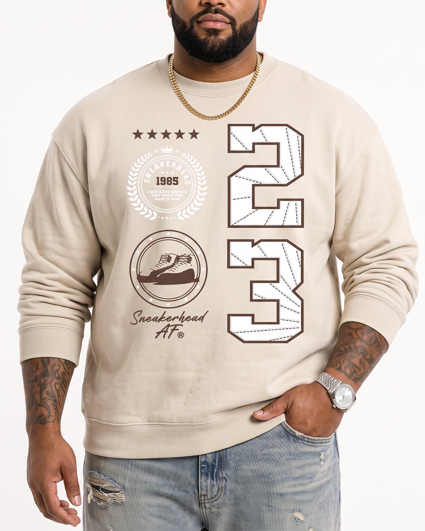 A man wearing a beige crewneck sweatshirt with a graphic print featuring the number 23, a laurel wreath, a sneaker, and the text 'Sneakerhead AF'.