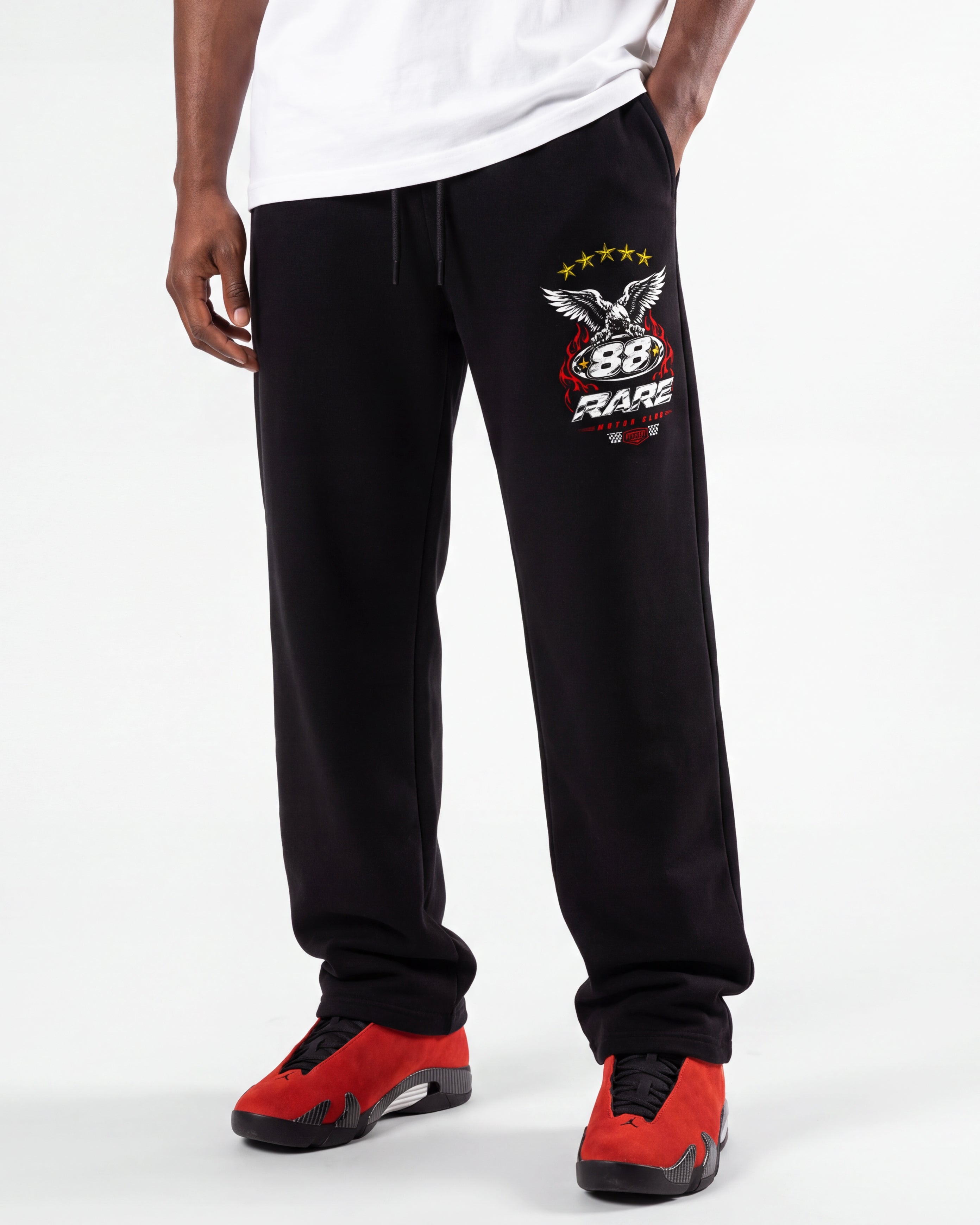 Black sweatpants with a prominent 88 RACE logo on the left thigh, worn by a model with a white t-shirt and red sneakers against a white studio background.