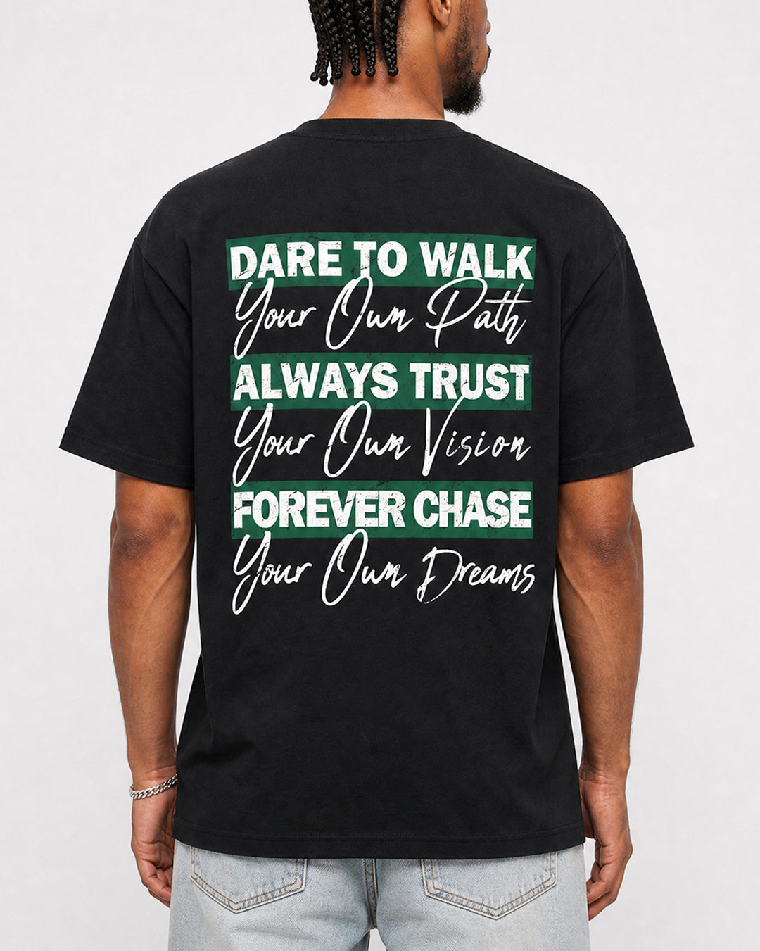 A man wearing a black t-shirt from the back, featuring a motivational quote printed in white and green text. The text reads: 'DARE TO WALK Your Own Path, ALWAYS TRUST Your Own Vision, FOREVER CHASE Your Own Dreams'.