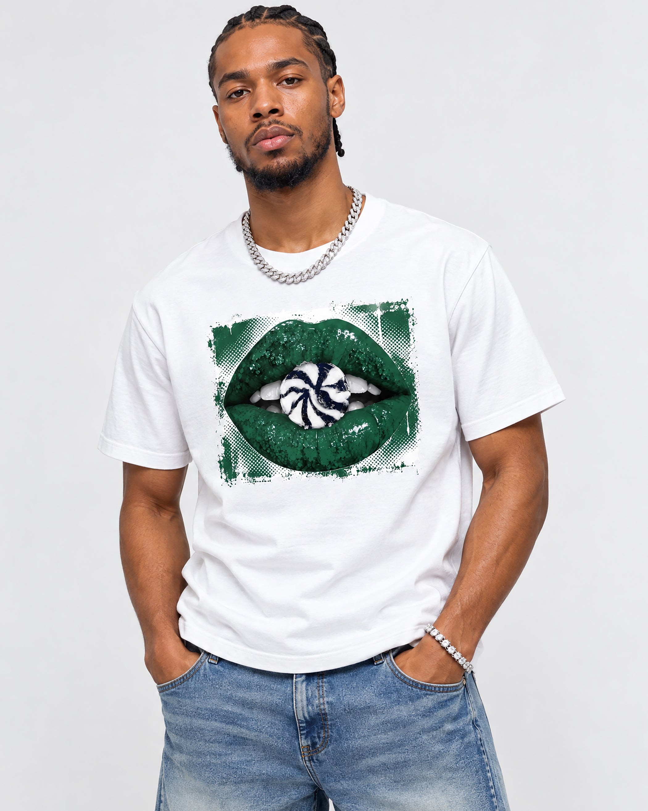 A man wearing a white crewneck t-shirt with a green lips graphic on the front, paired with blue jeans and silver jewelry, against a light gray background.