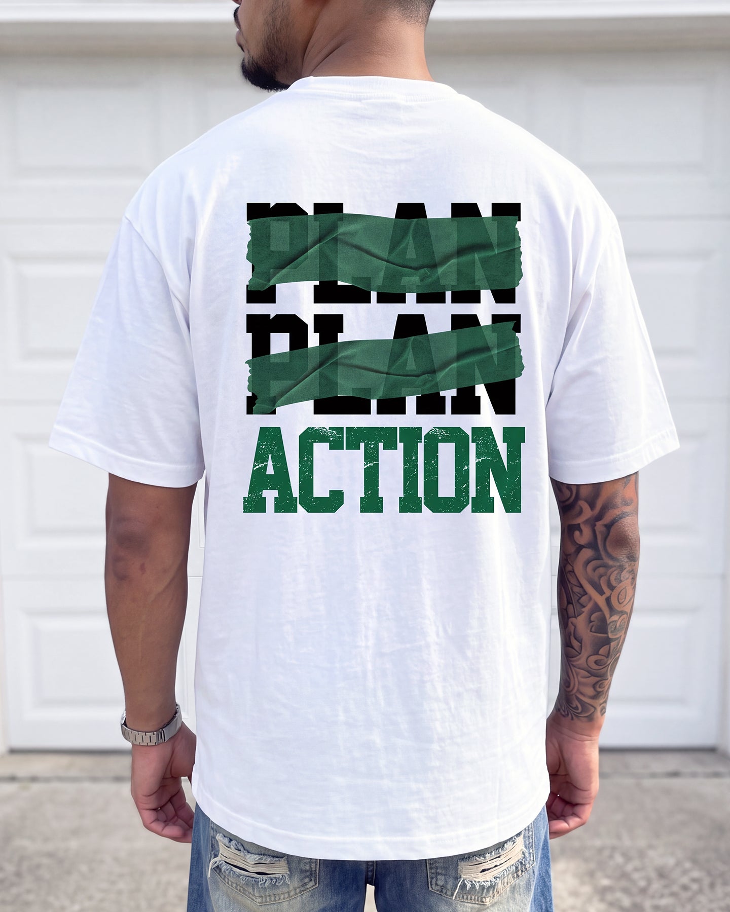 A man viewed from behind wearing a white t-shirt with a graphic on the back that reads 'PLAN PLAN ACTION' in black and green block letters, with the middle words covered by green tape graphics.
