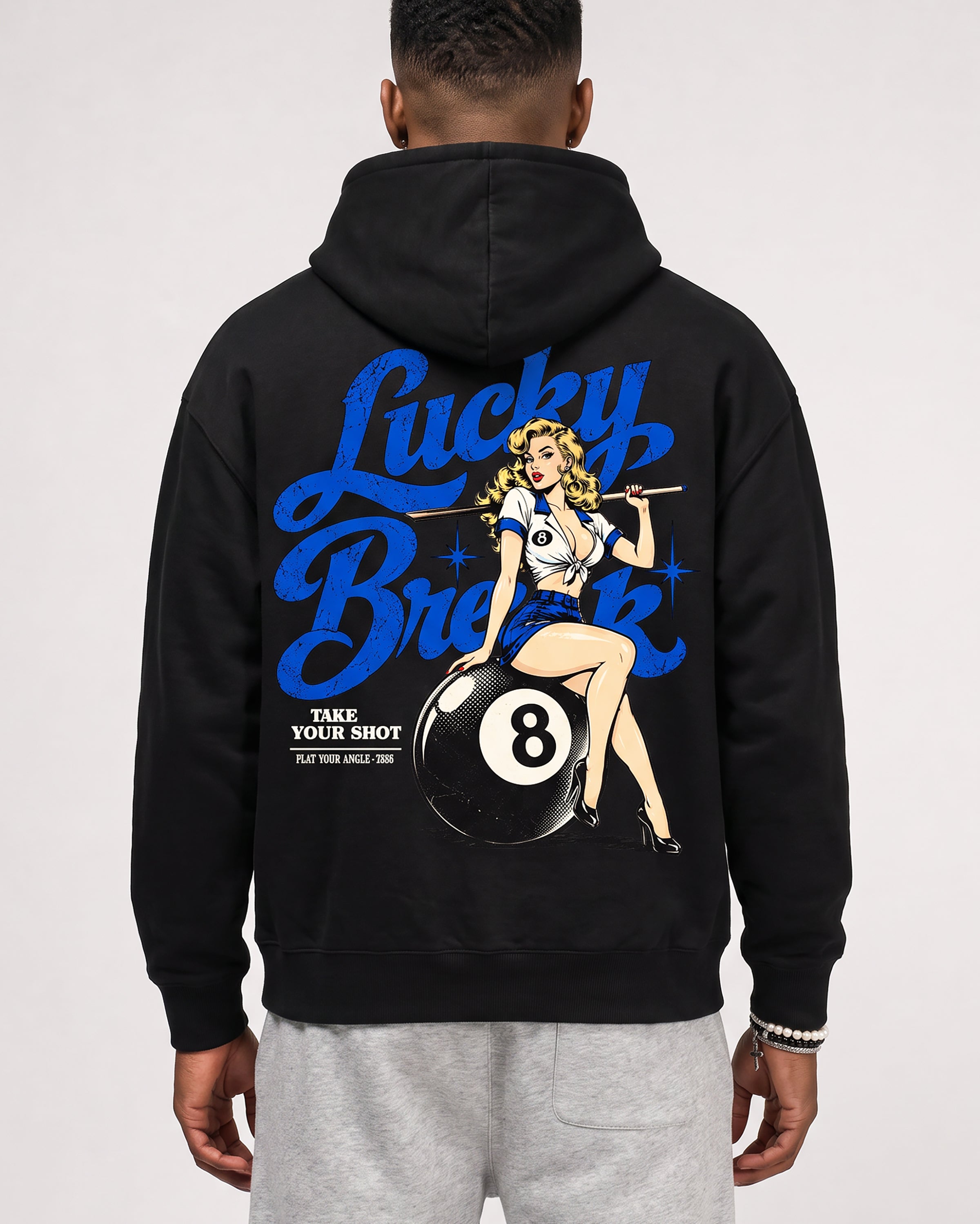 A man viewed from the back wearing a black hoodie with a large graphic print on the back. The print features blue 'Lucky Break' lettering, a pin-up style illustration of a woman, and a black 8-ball with the text 'TAKE YOUR SHOT'.