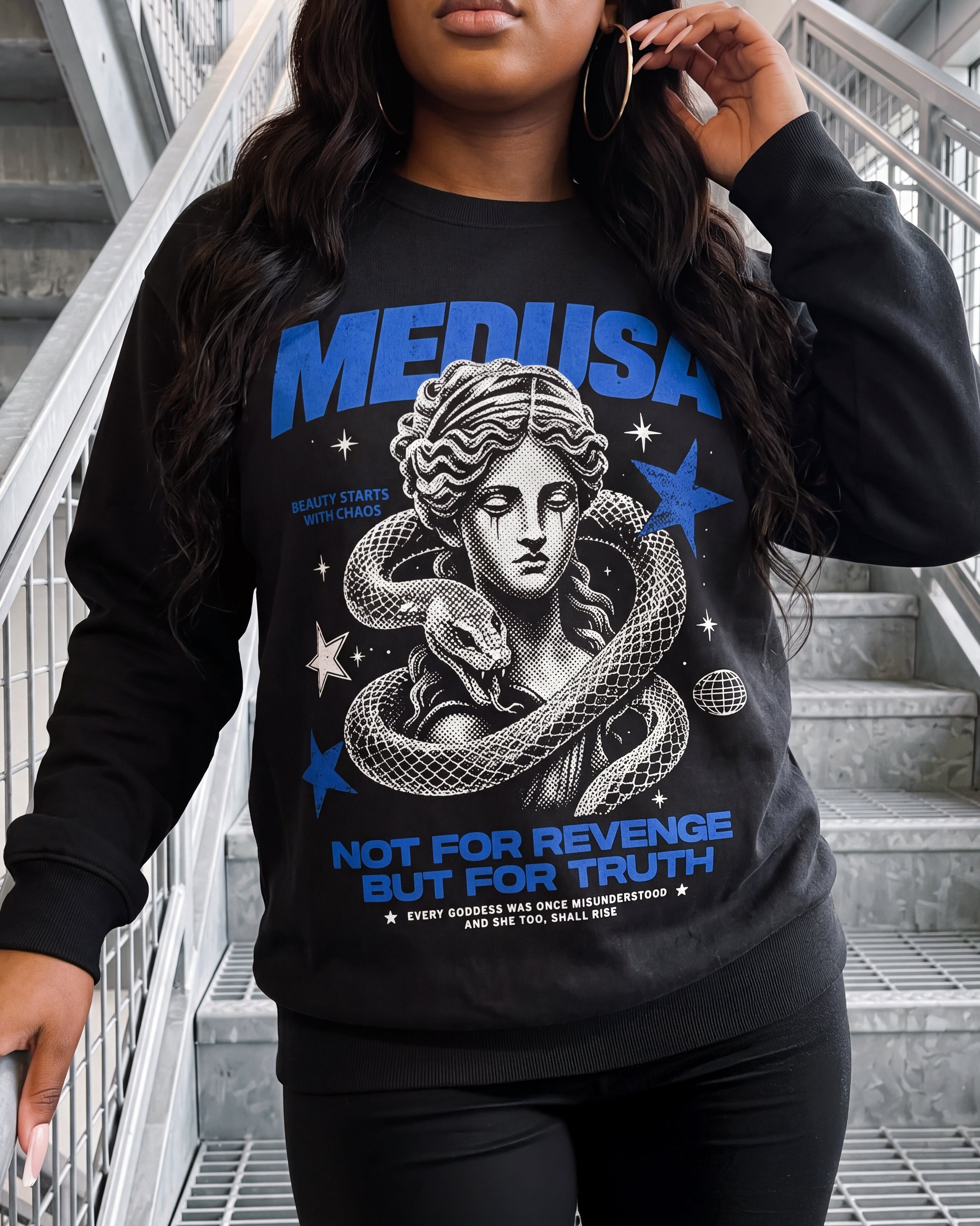 A woman wearing a black long-sleeve sweatshirt with a blue and white graphic print featuring Medusa and the text 'MEDUSA NOT FOR REVENGE BUT FOR TRUTH', photographed on an outdoor staircase.