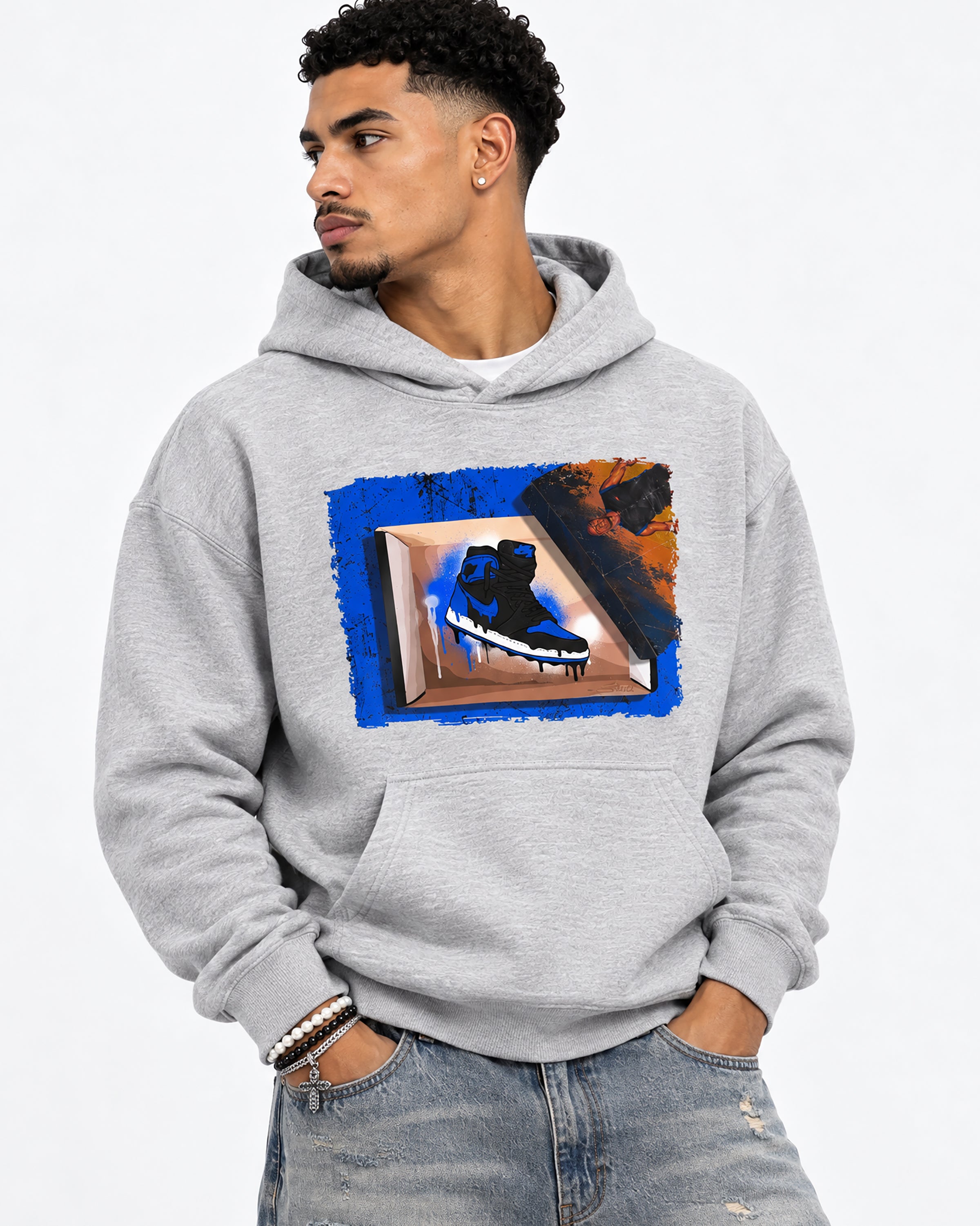 A man wearing a light gray pullover hoodie with a colorful graphic print on the front, paired with distressed blue jeans, photographed against a clean white background.