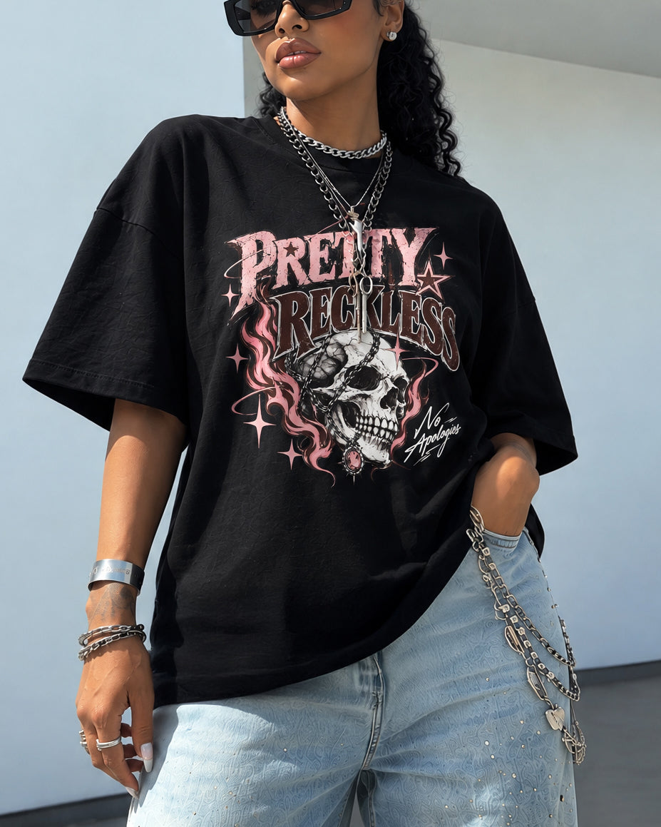 A woman wearing a black oversized graphic T-shirt with a pink and white skull design and the text 'PRETTY RECKLESS' and 'New Age Witches'.