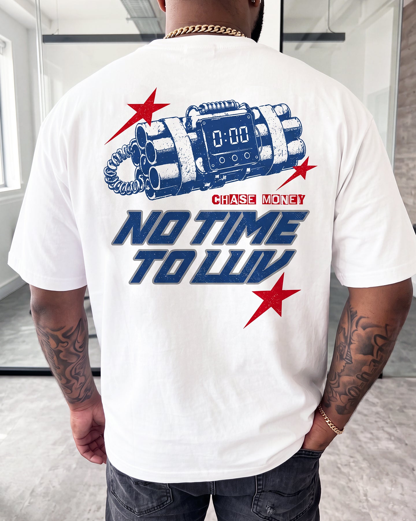 A man wearing a white t-shirt with a large blue and red graphic on the back, featuring a toy bomb design and the text 'CHASE MONEY' and 'NO TIME TO LUV'.