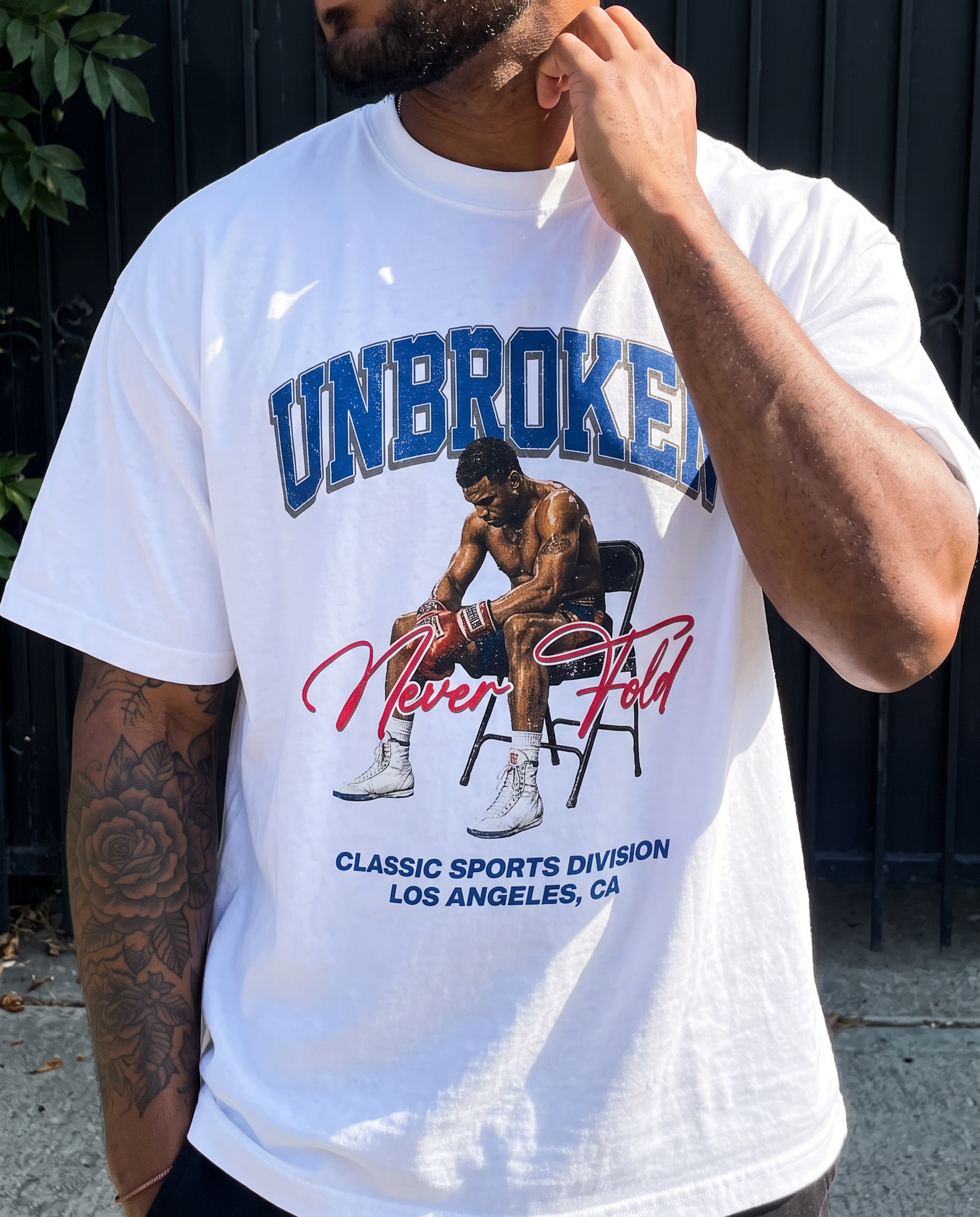 A man wearing a white graphic t-shirt with a boxing design and the text 'UNBROKEN Never Fall' and 'CLASSIC SPORTS DIVISION LOS ANGELES, CA'.