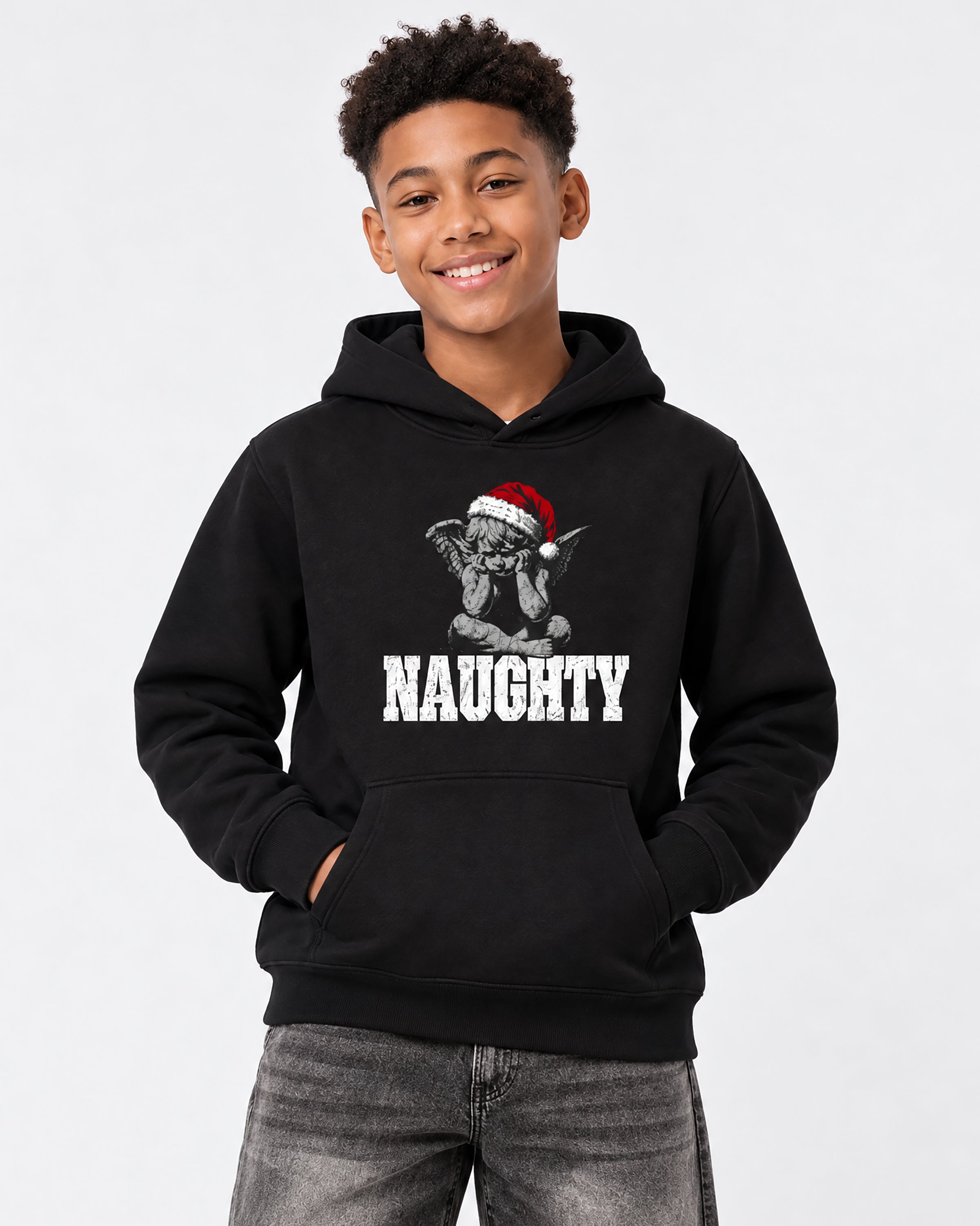 A smiling young man wearing a black pullover hoodie with a graphic of a goblin in a Santa hat and the word 'NAUGHTY' in white, paired with gray jeans, against a light gray background.