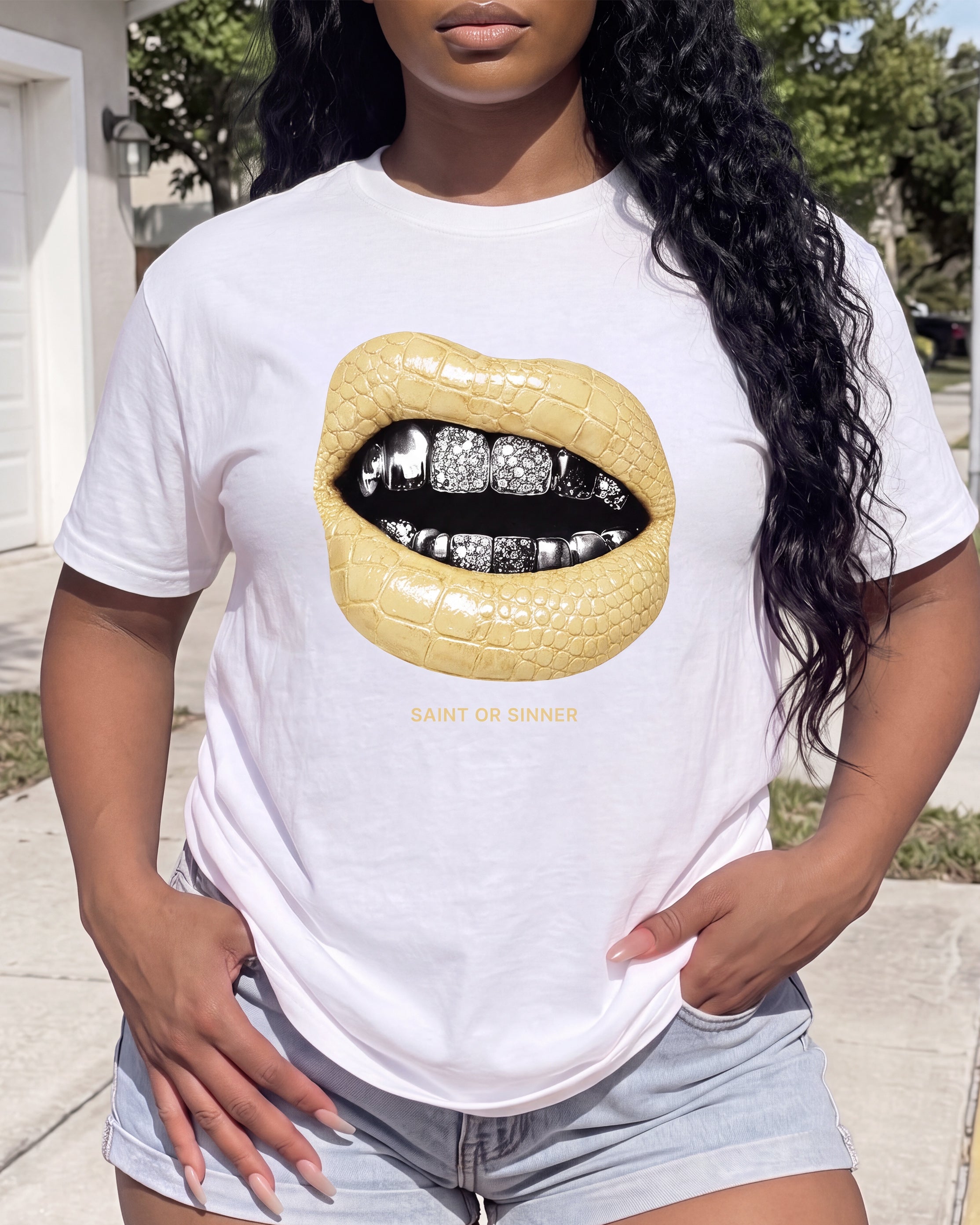 A woman wearing a white graphic t-shirt featuring a large crocodile-textured yellow lip design with black and silver teeth, and the text 'SAINT OR SINNER' printed below.