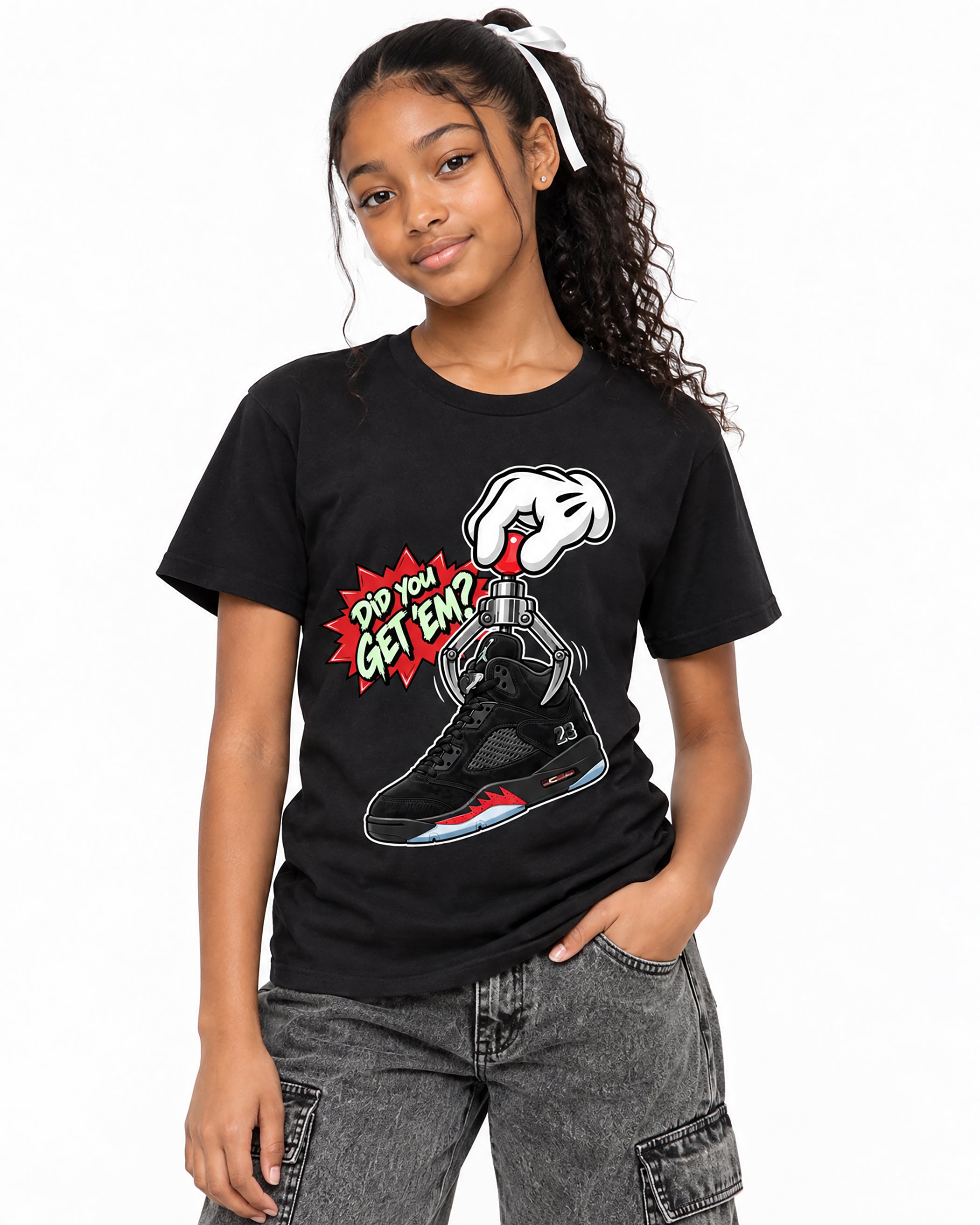 A young girl with curly hair wearing a black graphic t-shirt and gray cargo pants, standing against a plain white background.
