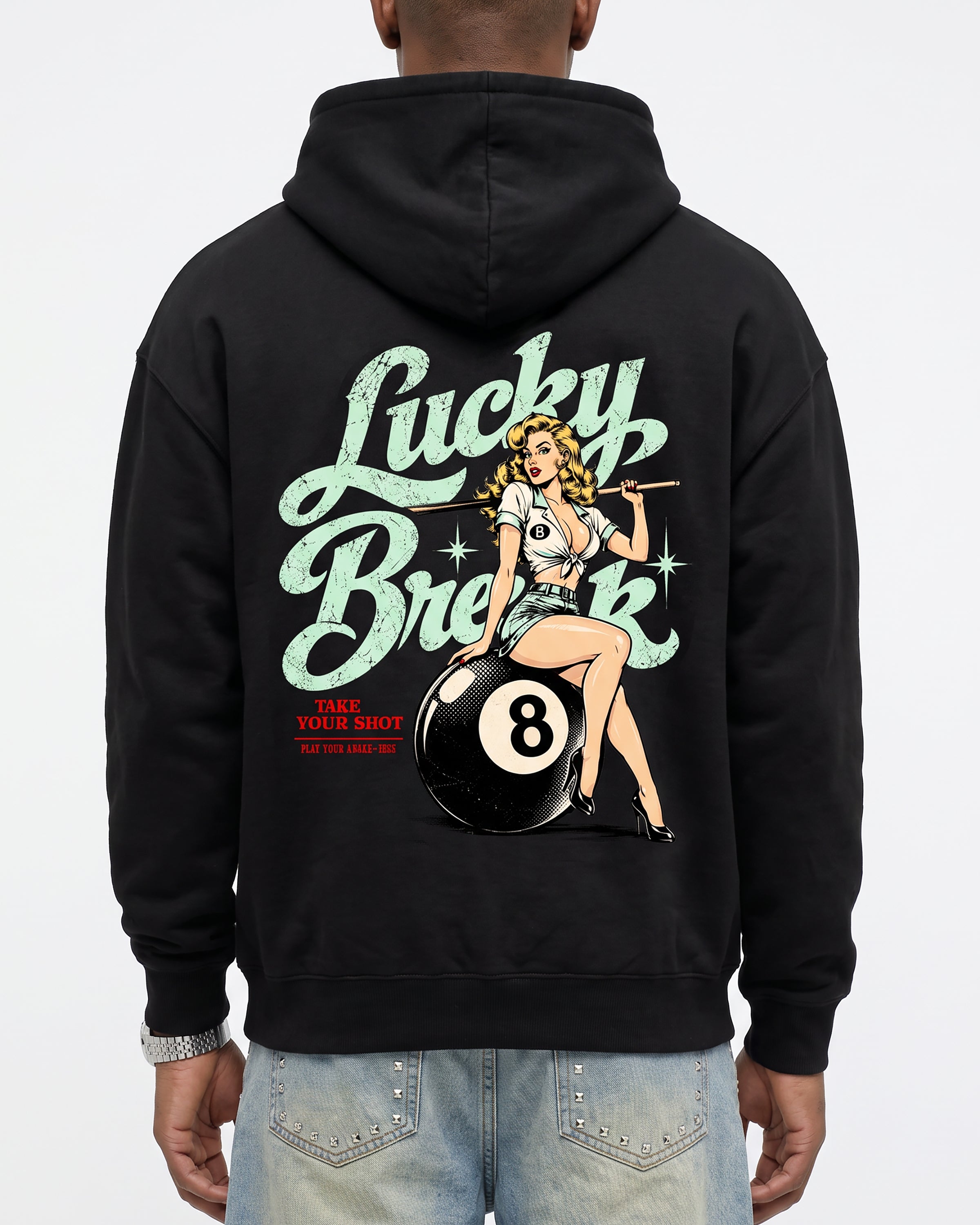 A person shown from the back wearing a black hoodie with a large retro-style back graphic featuring the words 'Lucky Break,' a pin-up illustration, and a 8-ball pool cue. The person is also wearing light blue jeans against a plain light gray studio background.