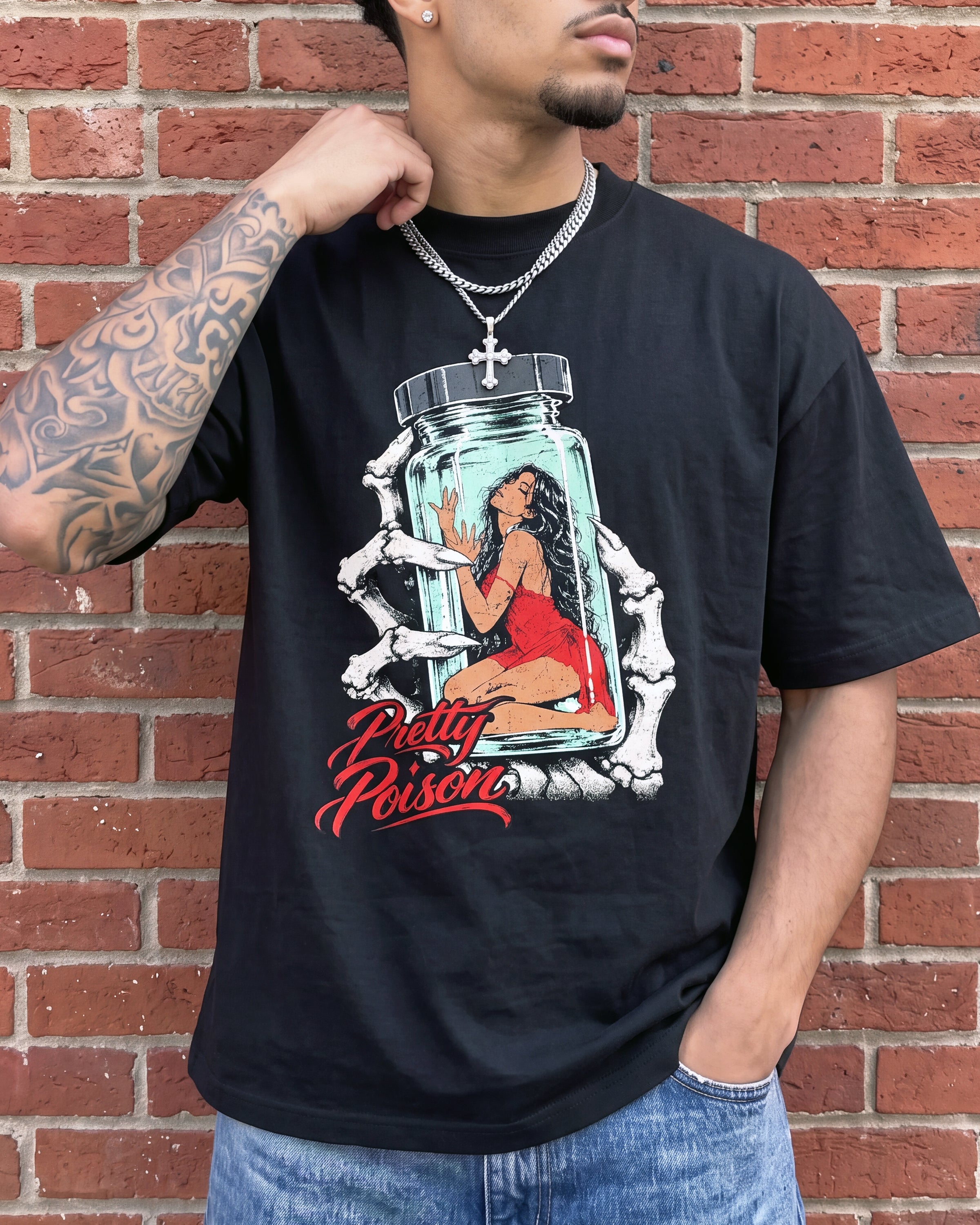 A man wearing a black graphic t-shirt with a 'Pretty Poison' design, standing against a red brick wall.