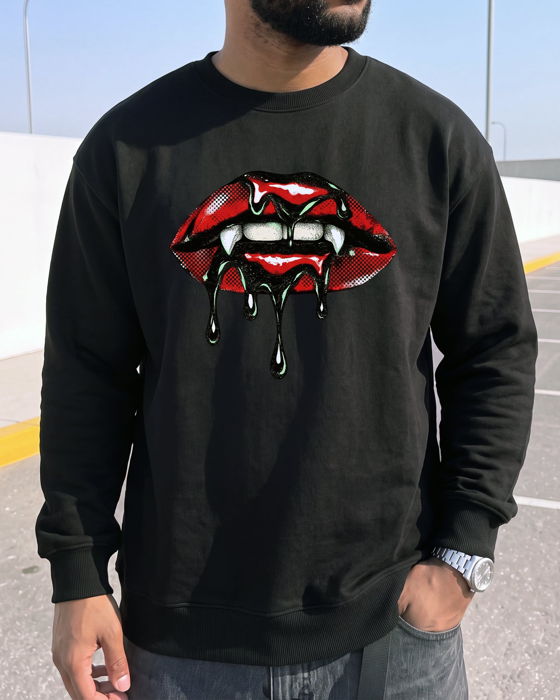 A man wearing a black crewneck sweatshirt with a graphic of dripping red lips with white fangs and black blood-like drips, set against an outdoor background.