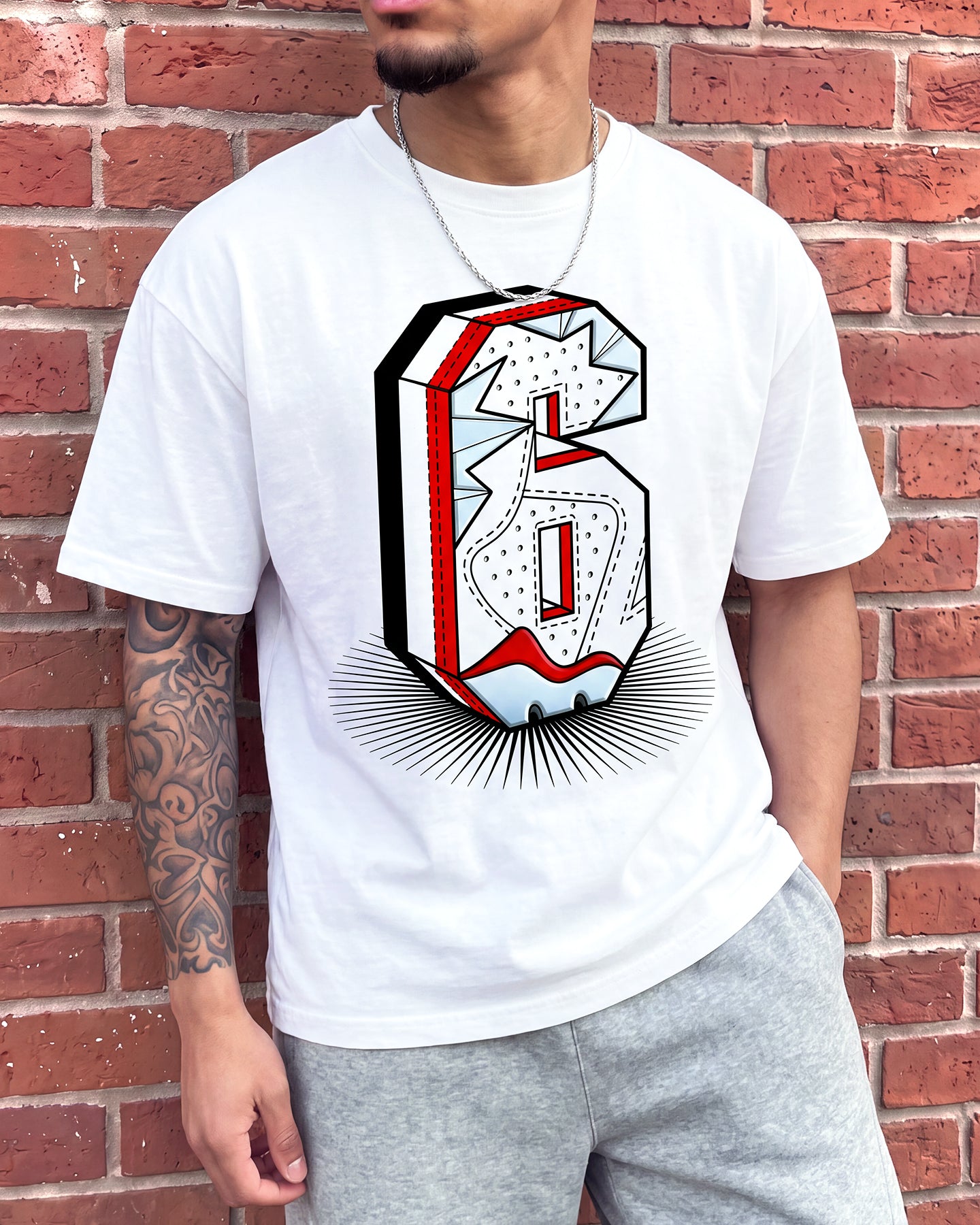 A man wearing a white graphic t-shirt with a stylized 3D number 6 design in red, black, and white, standing against a red brick wall.