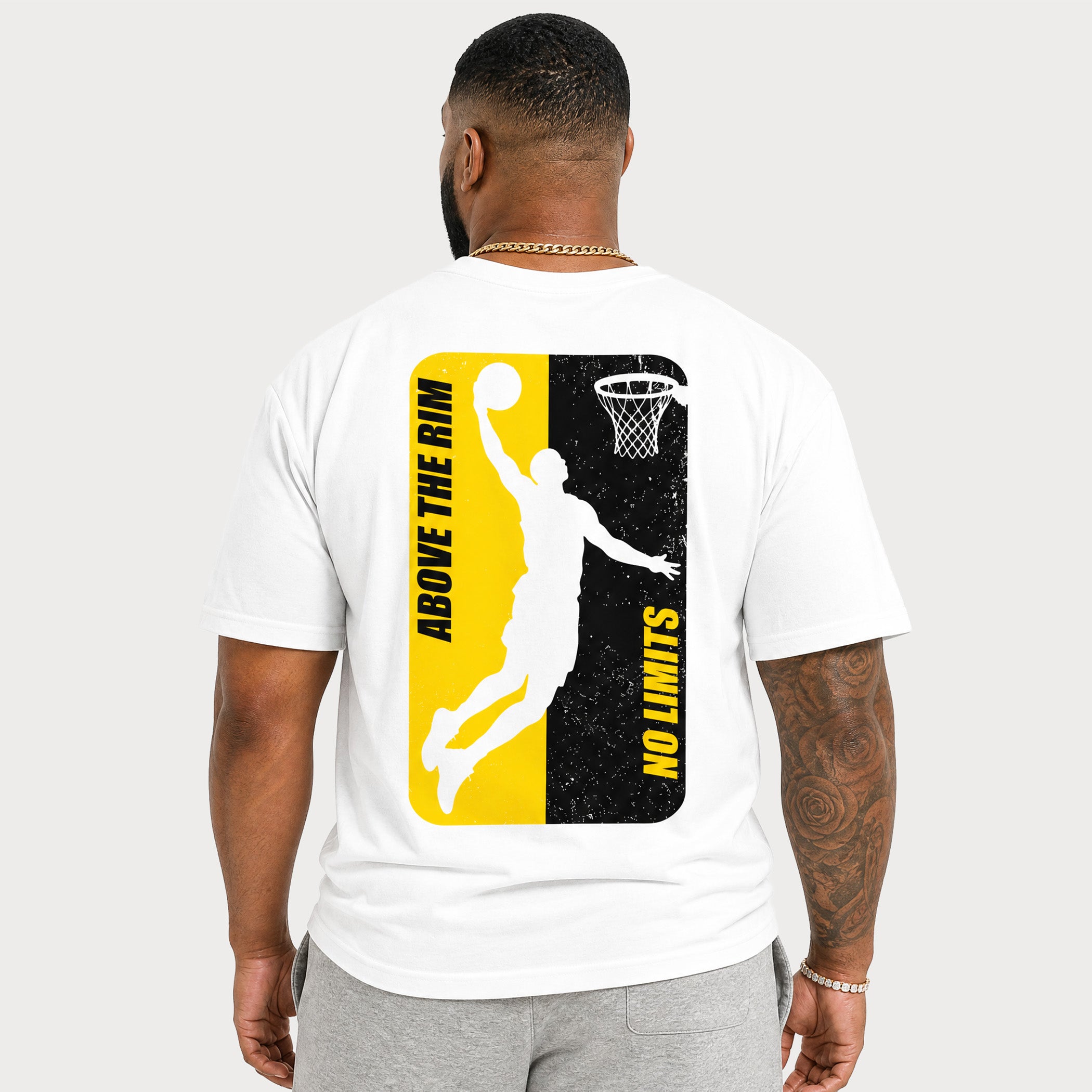 A man viewed from the back wearing a white t-shirt with a large basketball graphic on the back. The graphic features a split yellow and black design with a white silhouette of a basketball player dunking and the text 'ABOVE THE RIM' and 'NO LIMITS'.