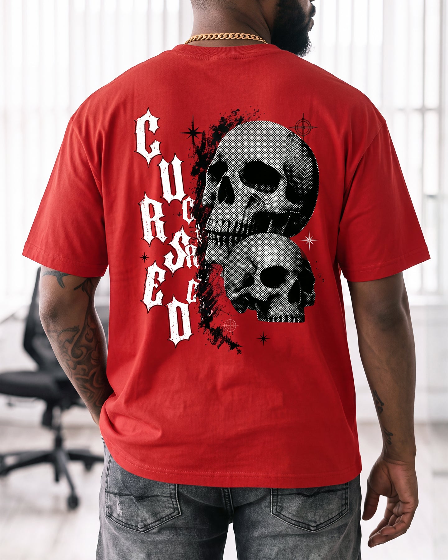 A man wearing a red t-shirt with a large graphic on the back featuring two black and white skulls and the word 'Cursed' in white gothic lettering, shown from behind.