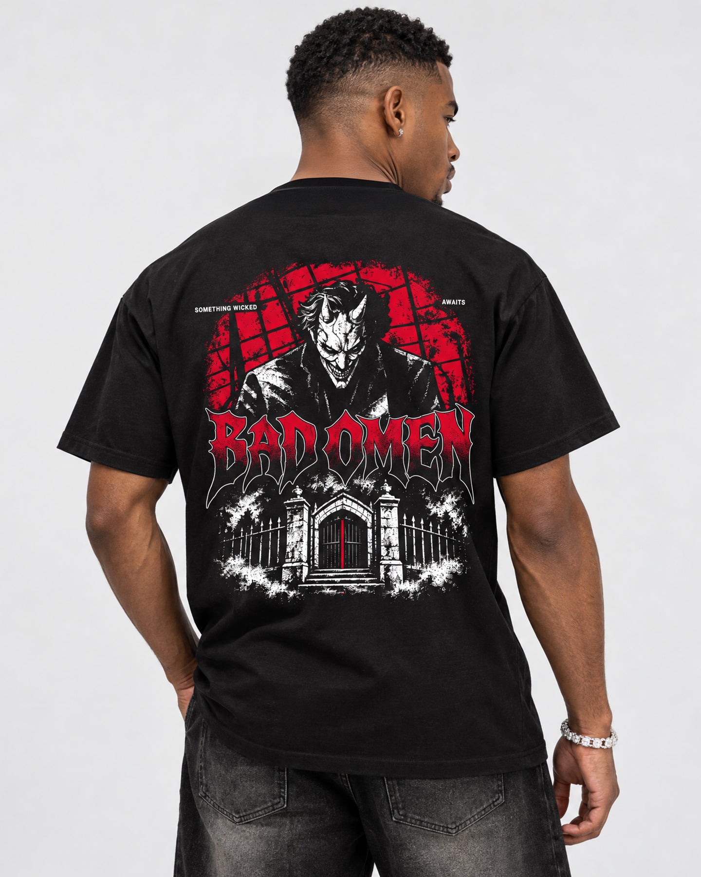 A man wearing a black t-shirt from the back, featuring a large graphic print of a devil-like character and the text 'BAD OMEN' in red and white, set against a plain light gray background.
