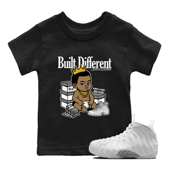 Built Different Since Birth baby and kids t-shirt crafted for little sneakerheads to shine with the Air Foamposite One Triple White sneakers, displayed in Black 1.