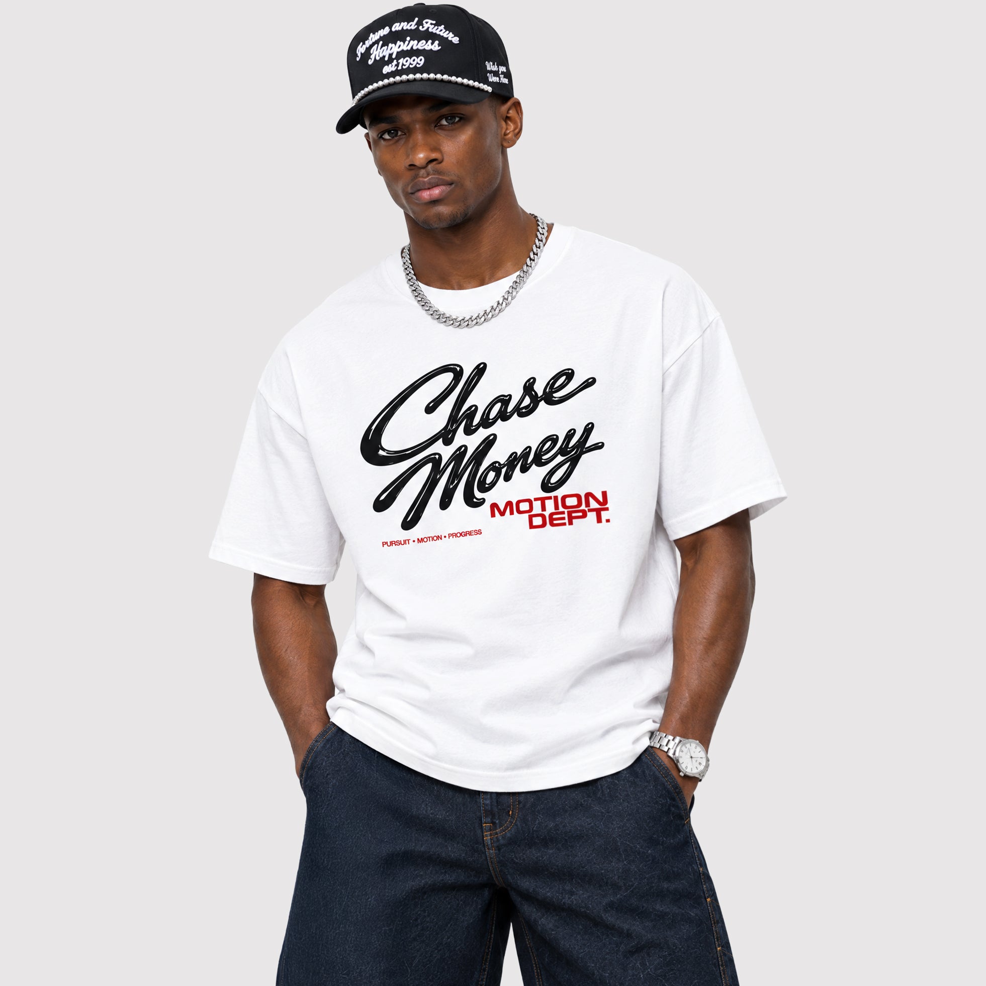A man wearing a white t-shirt with a black 'Chase Money' script and red 'MOTION DEPT.' text, paired with a black cap and dark jeans, against a light gray background.