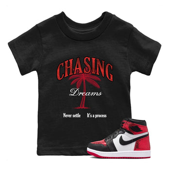 Chasing Dreams baby and kids t-shirt crafted for little sneakerheads to shine with the Air Jordan 1 Ruby sneakers, displayed in Black 1.