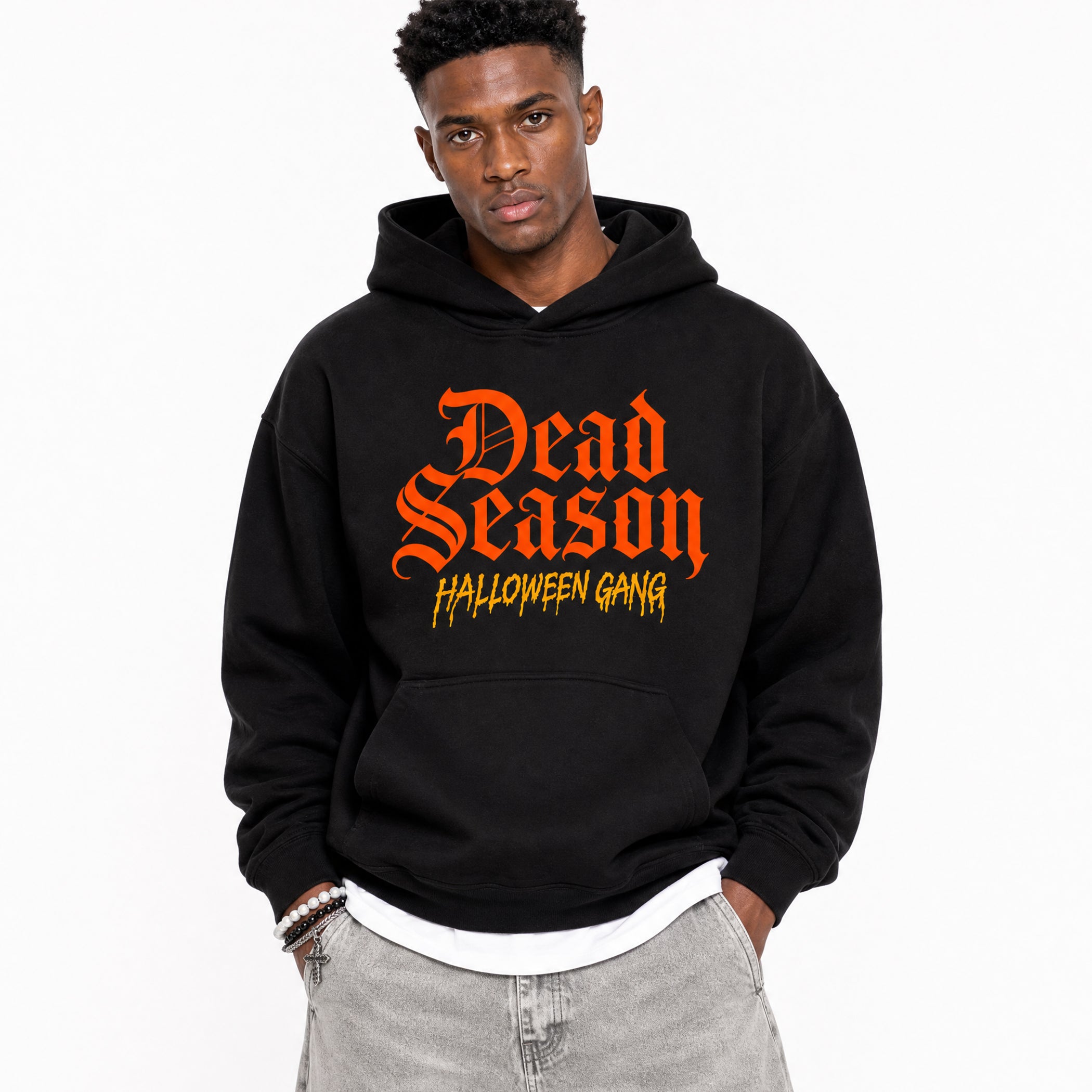 A man wearing a black pullover hoodie with 'Dead Season' in orange gothic lettering and 'HALLOWEEN GANG' in yellow text on the front, paired with light gray jeans against a plain white background.