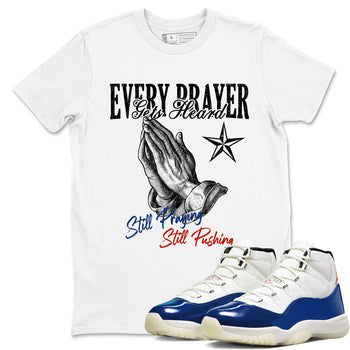 White t-shirt with praying hands graphic and text, paired with blue and white sneakers.