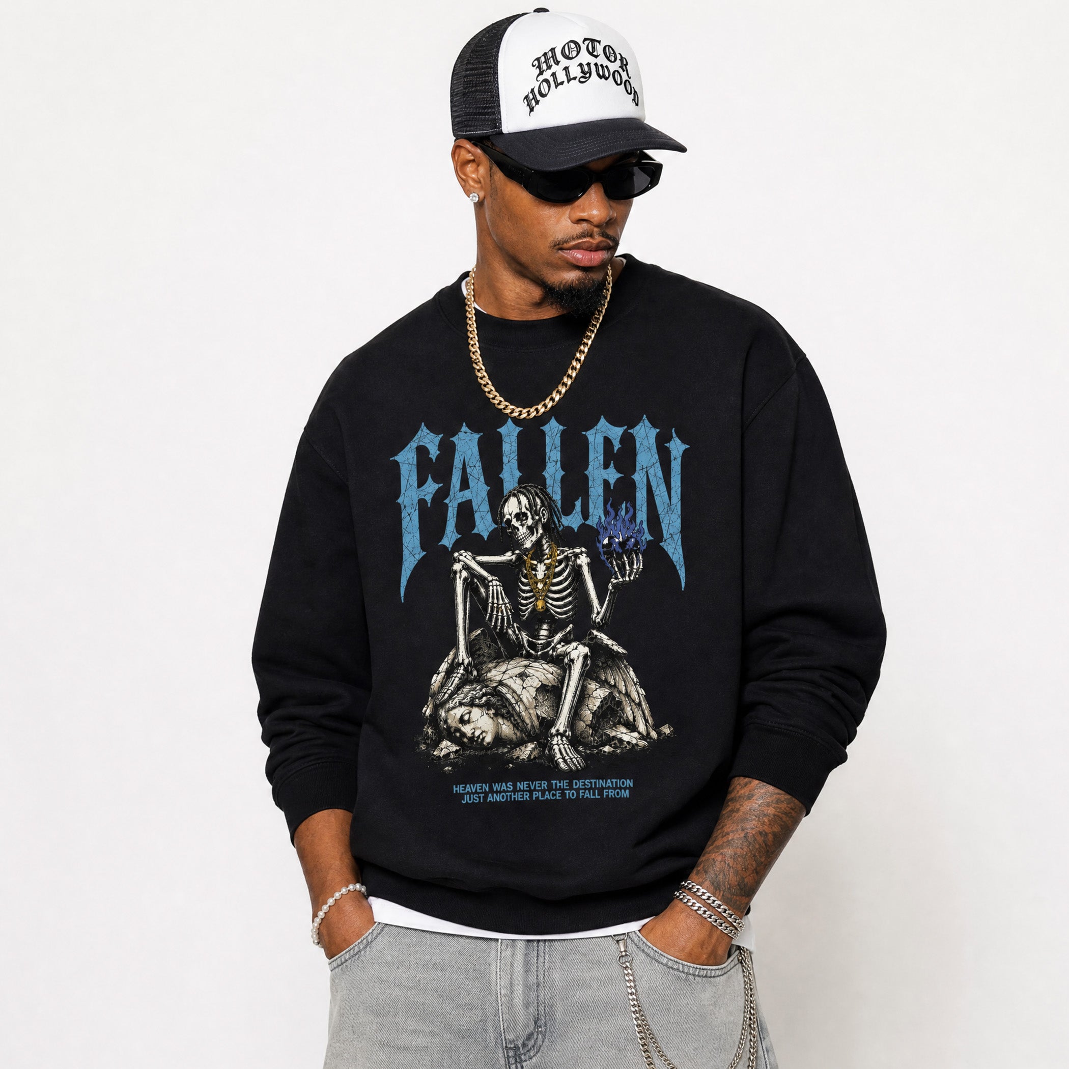 A man wearing a black crewneck sweatshirt with a blue and white graphic print of a skeleton and the word 'FALLEN', paired with a black and white trucker hat, sunglasses, and a gold chain necklace, against a plain white background.