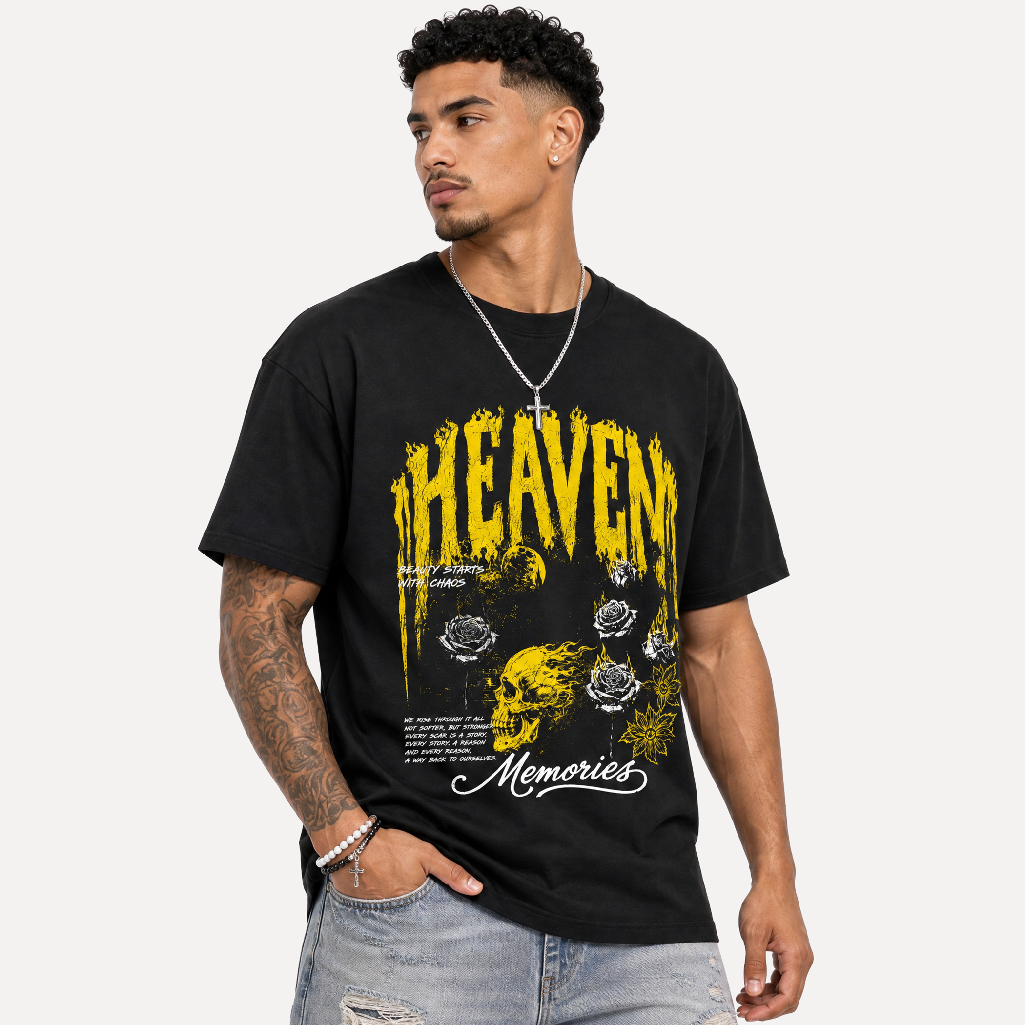 A man wearing a black graphic t-shirt with a yellow and white 'HEAVEN Memories' design, paired with light-wash distressed jeans and a silver necklace, set against a plain light gray background.