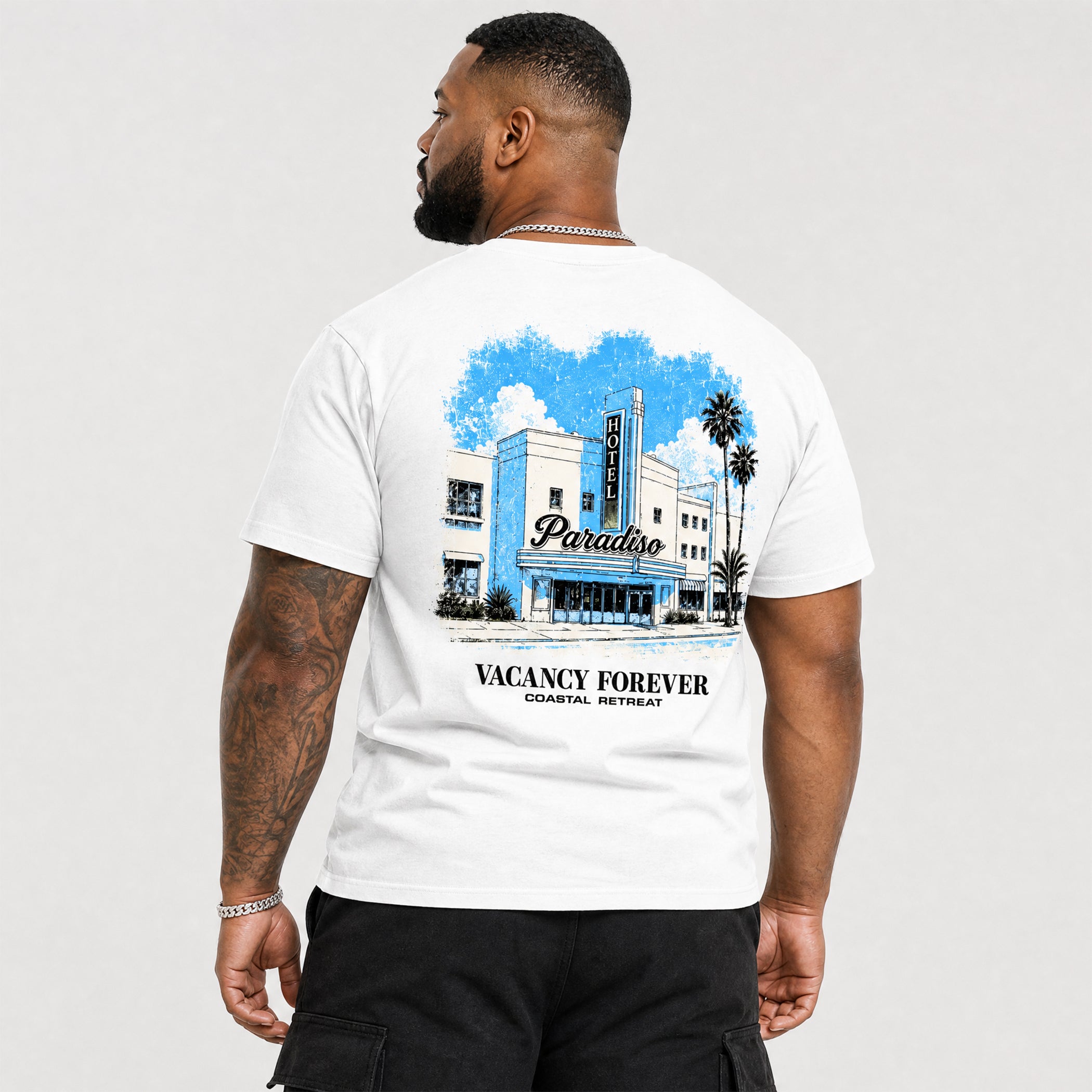 Man wearing a white t-shirt with a hotel paradiso graphic design on the back, featuring a building and text.