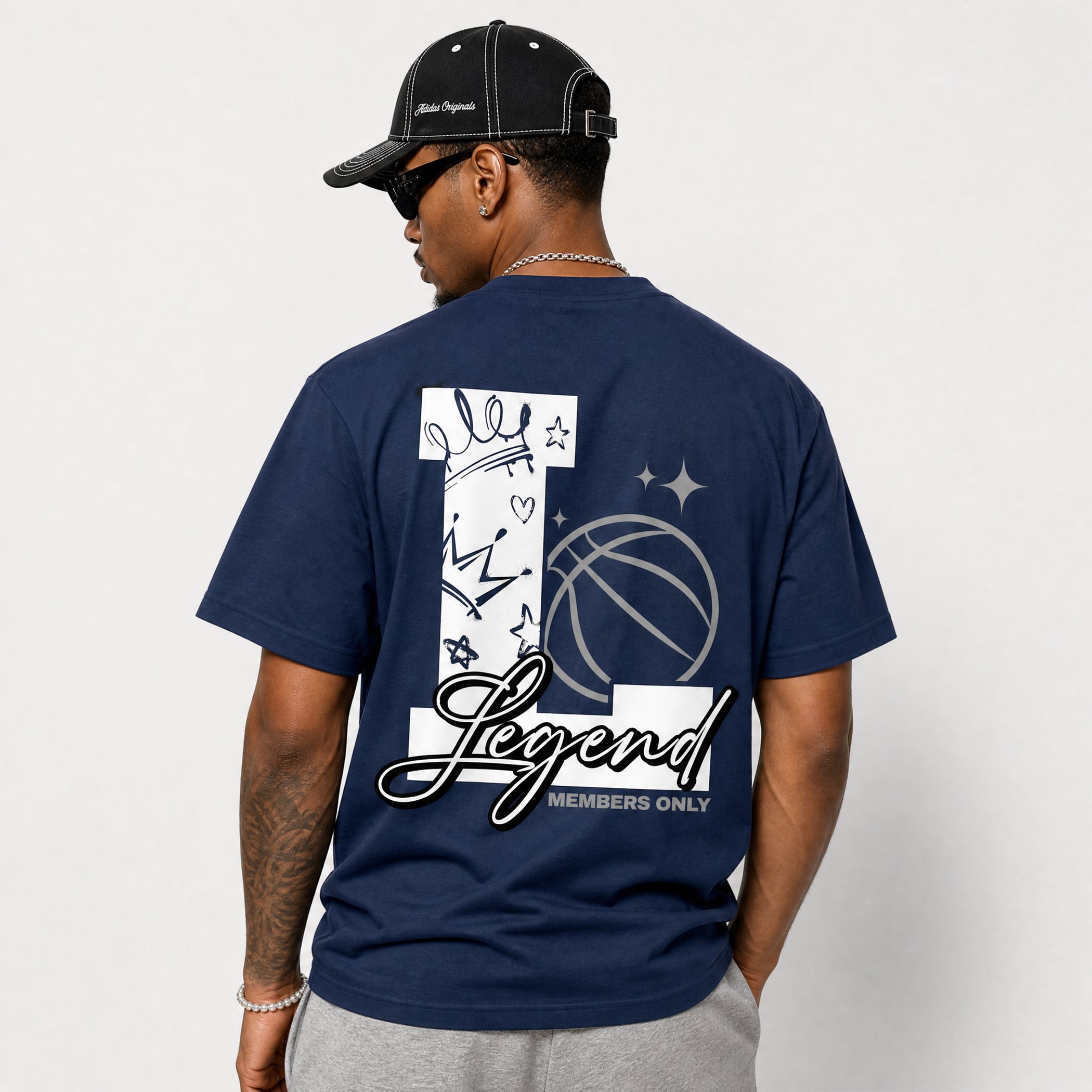 A man wearing a navy blue t-shirt from the back, featuring a large white graphic with a basketball, stars, and the word 'Legend' in script. He is also wearing a black baseball cap and sunglasses.