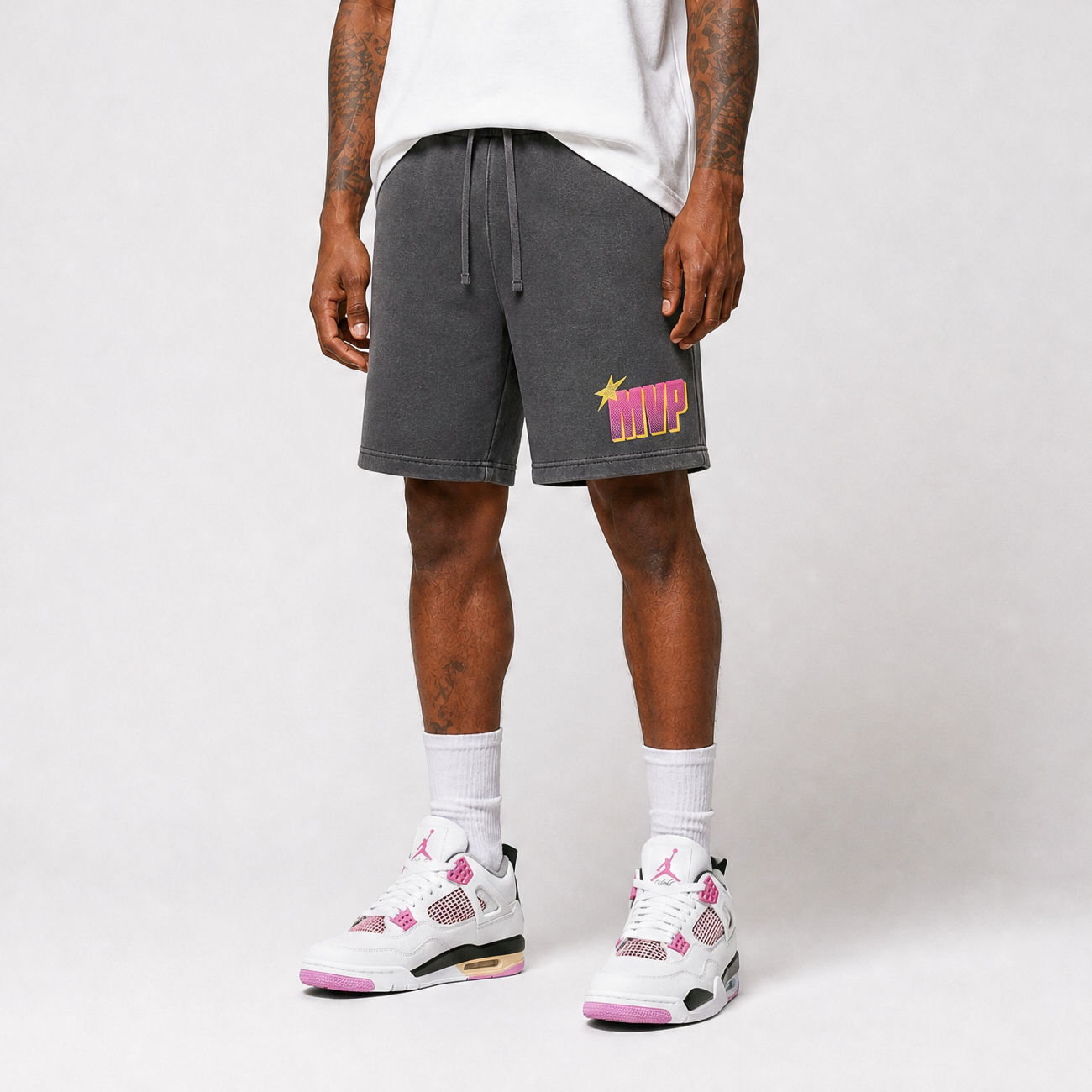 Person wearing gray shorts with a MVP colorful logo and white sneakers on a plain background