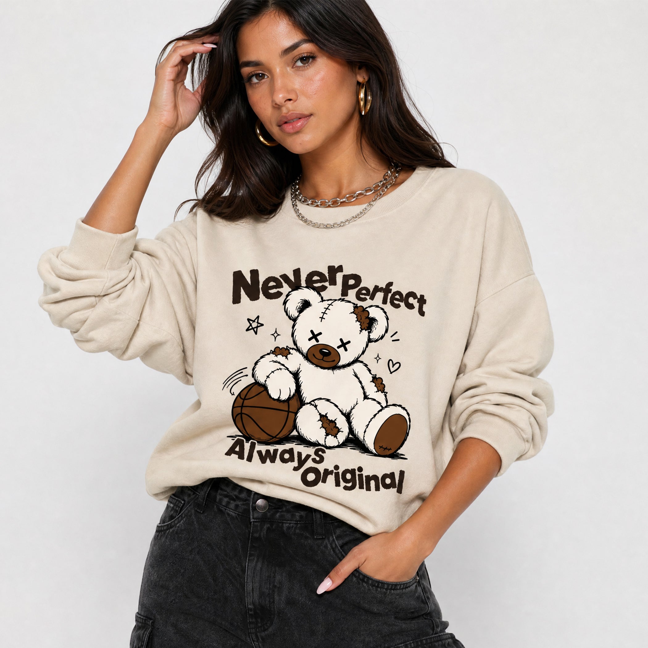 A woman wearing a beige crewneck sweatshirt with a graphic of a teddy bear holding a basketball and the text 'Never perfect Always original'.