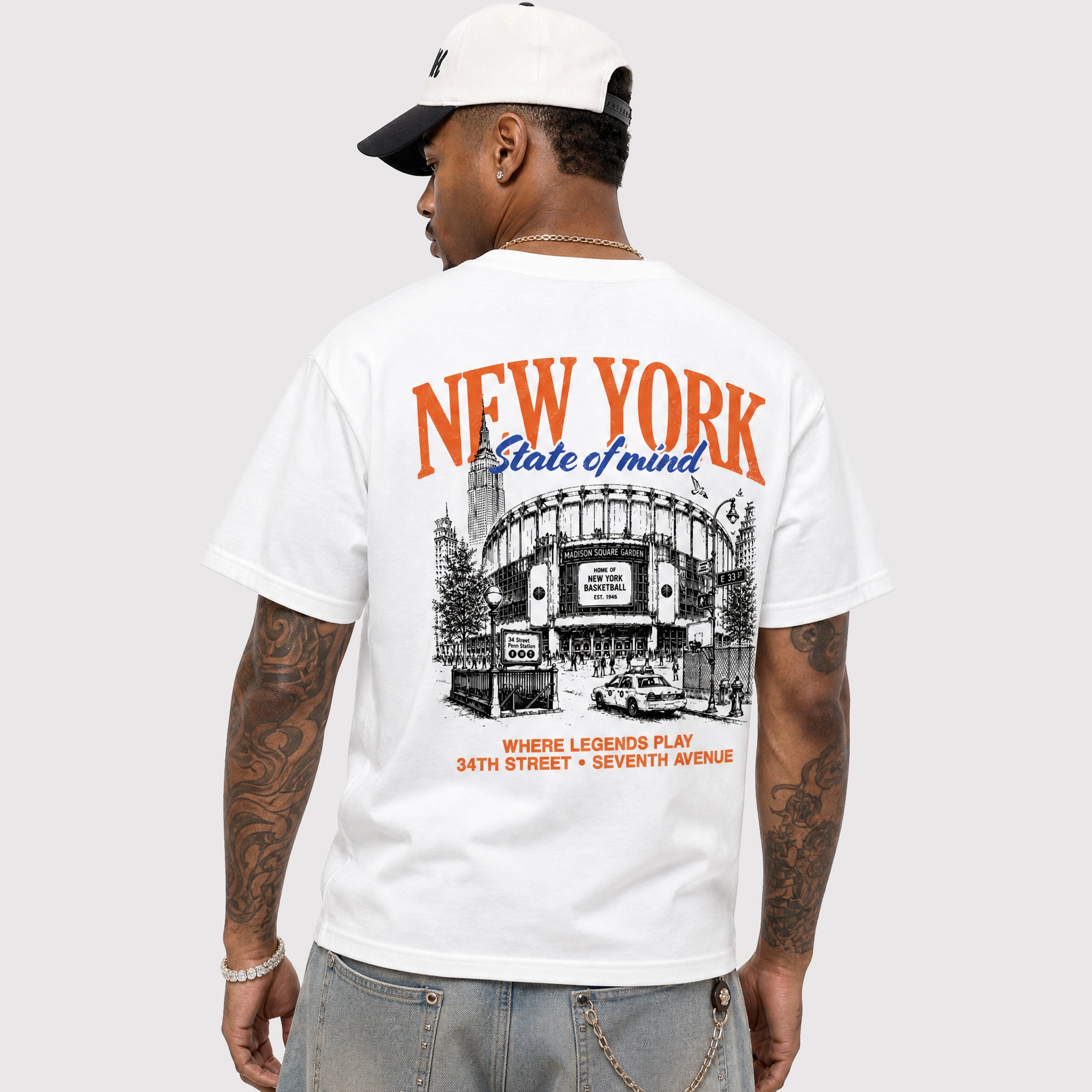 A man wearing a white t-shirt with a large back graphic that reads 'NEW YORK State of mind' above a black-and-white illustration of Yankee Stadium, paired with a white and black baseball cap and gray jeans, shown from the back against a light gray background.