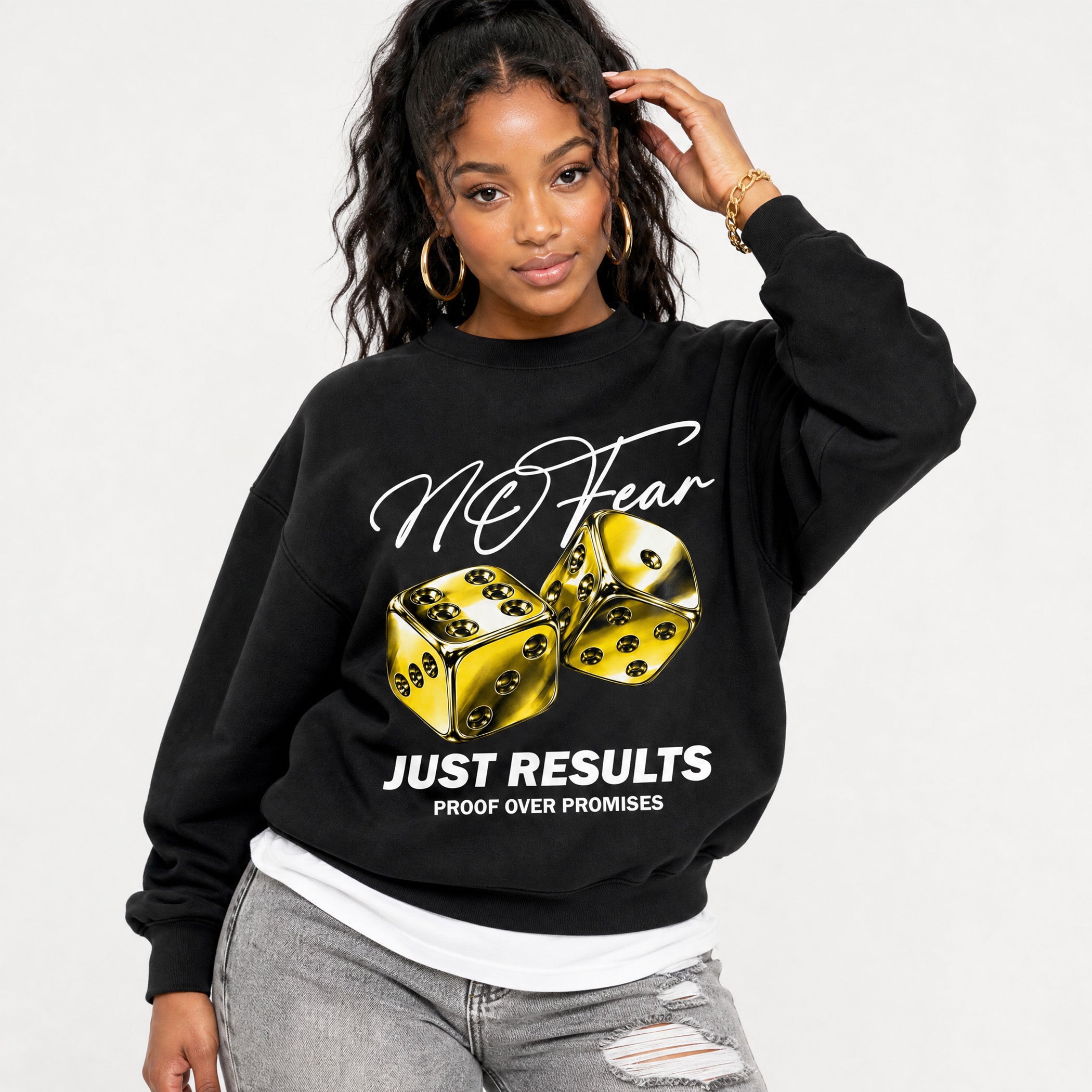 A woman modeling a black crewneck sweatshirt with a graphic print featuring gold dice and the text 'No Fear' and 'Just Results'.
