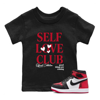 Self Love Club baby and kids t-shirt crafted for little sneakerheads to shine with the Air Jordan 1 Ruby sneakers, displayed in Black 1.