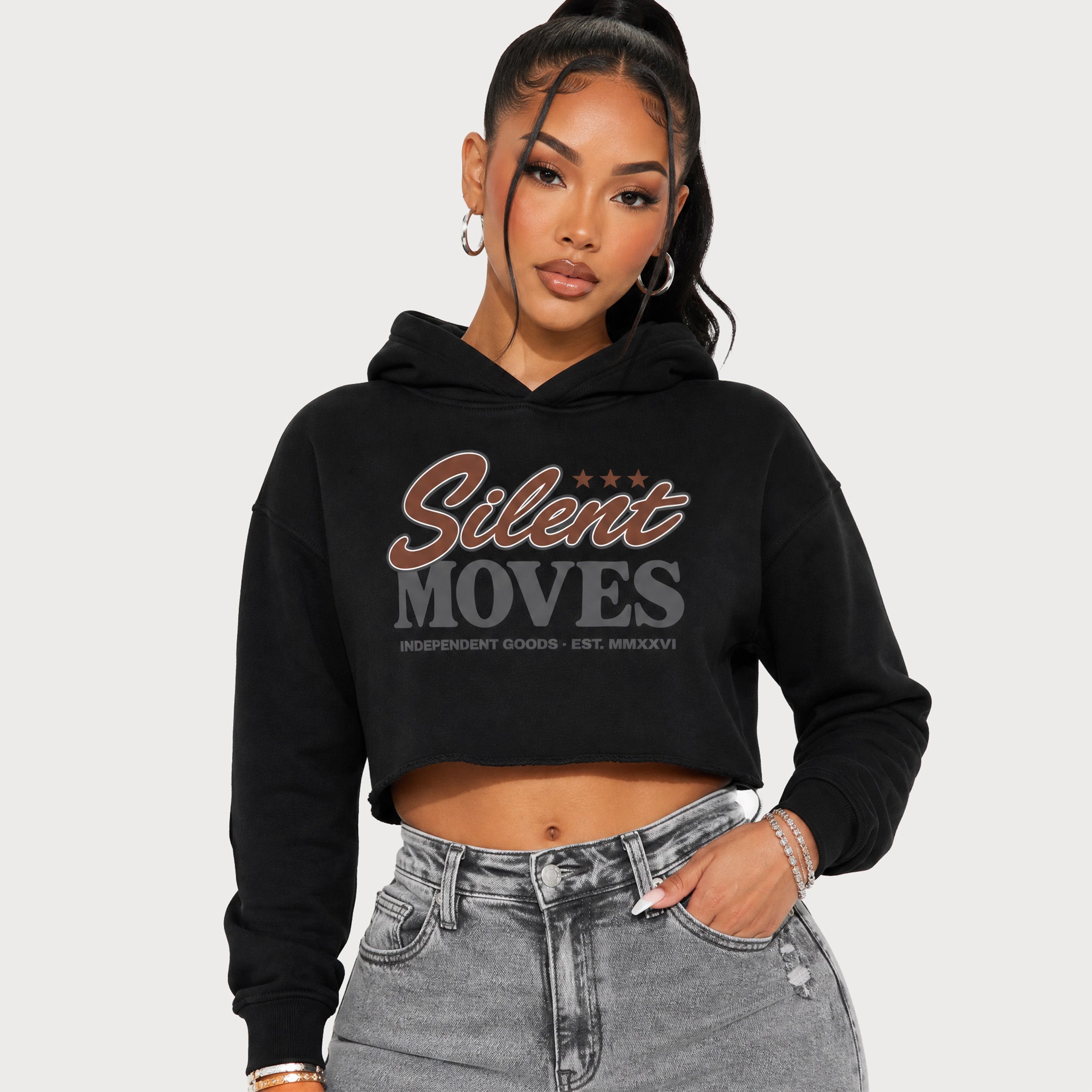 A woman modeling a black cropped hoodie with 'Silent Moves' printed on the front, paired with gray jeans, against a light gray background.