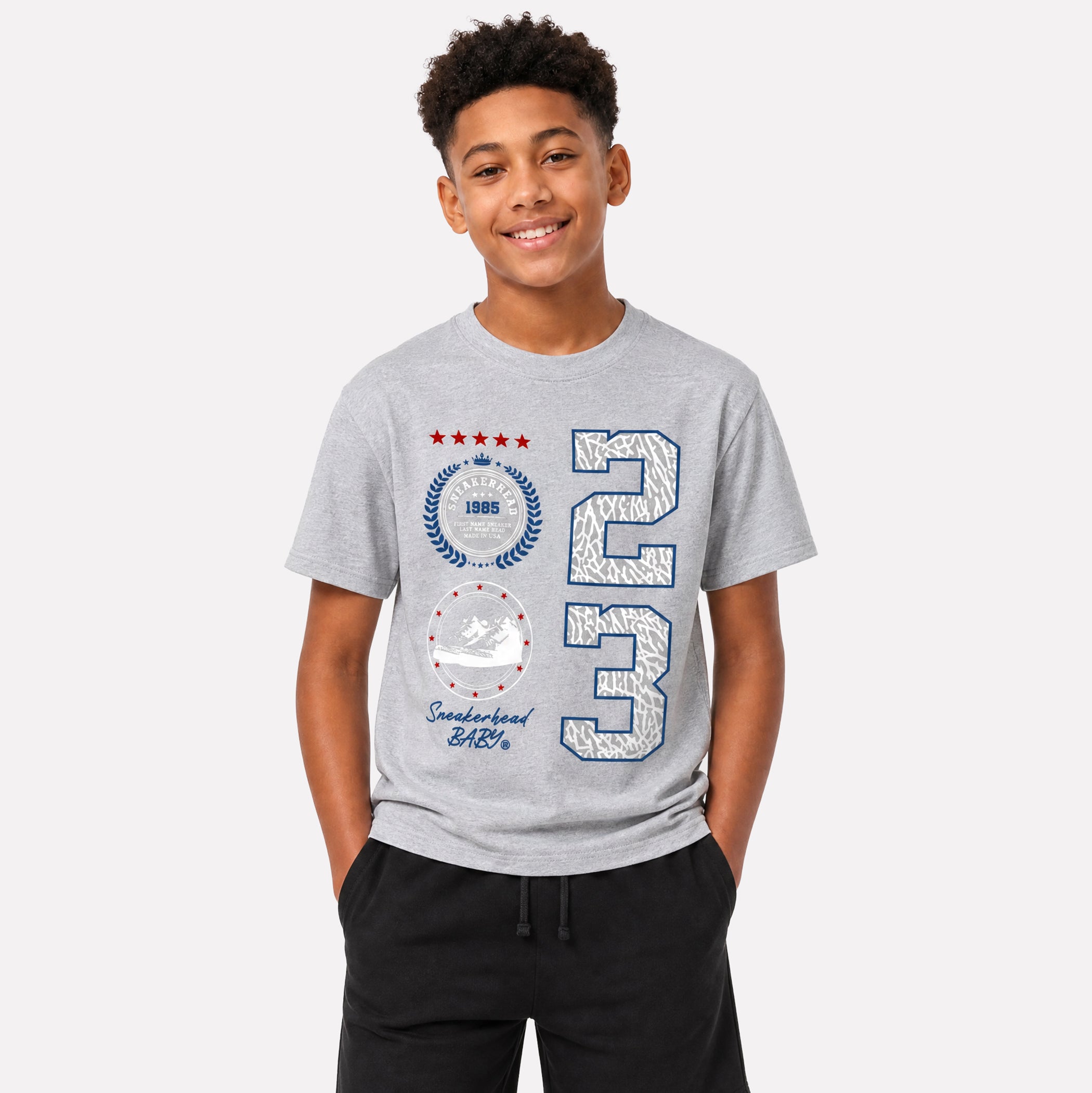 A young boy wearing a heather gray t-shirt with a distressed graphic of the number 23, a circular crest, and 'Smilebook Earth' text, paired with black sweatpants, against a light gray background.