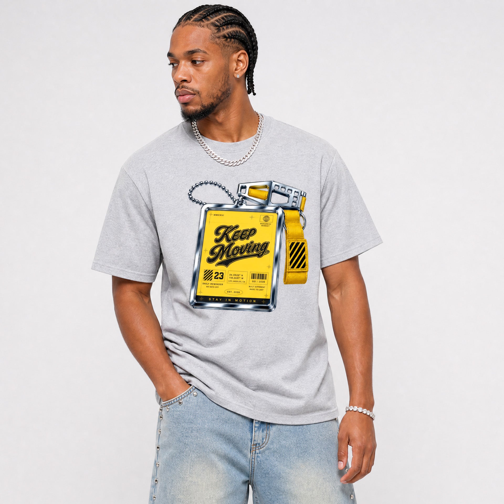 A man wearing a light gray crewneck t-shirt with a yellow and black graphic print of a 'Keep Moving' fuel can, paired with light wash blue jeans, against a plain light gray background.