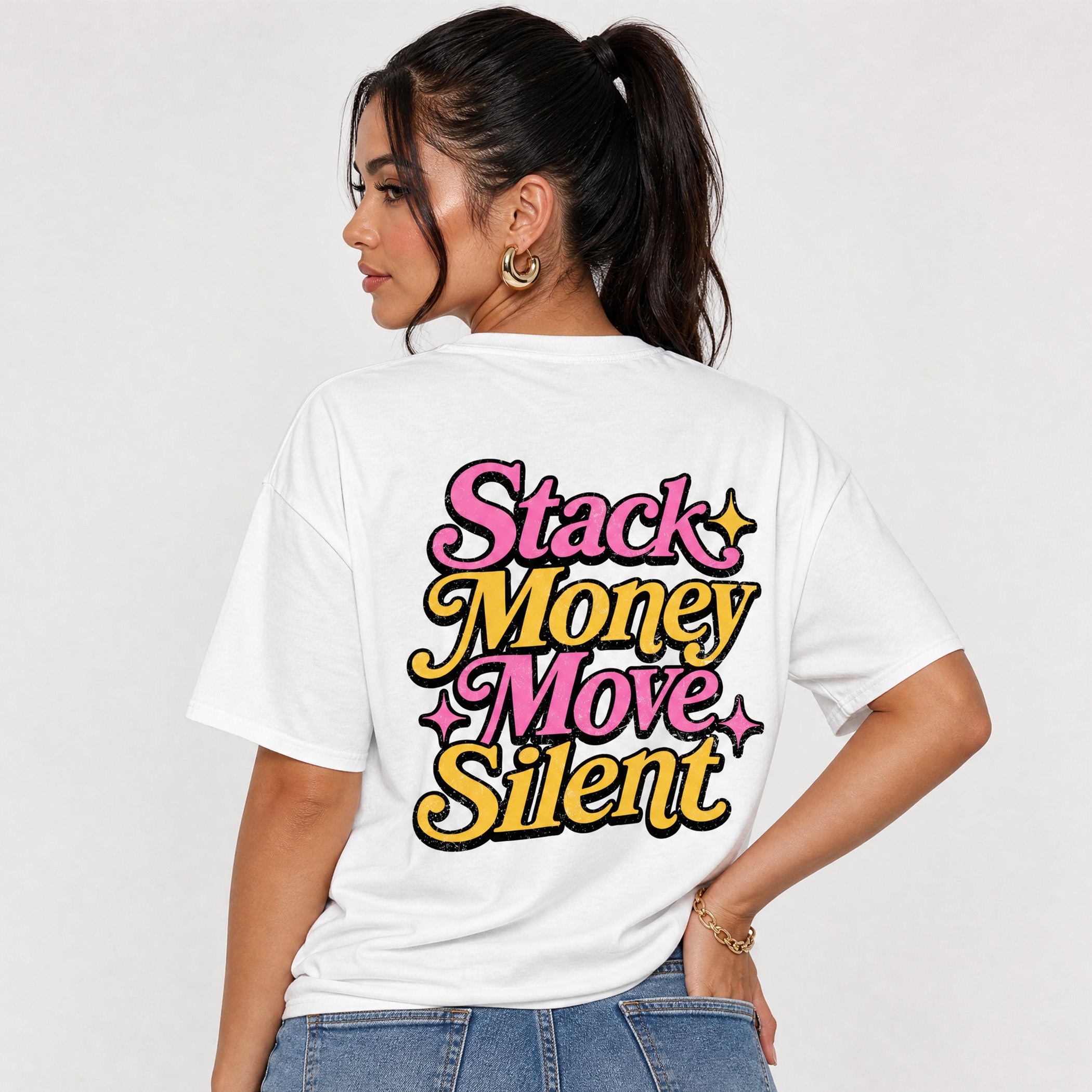 A woman shown from the back wearing a white graphic t-shirt with the text 'Stack Money Move Silent' in pink and yellow retro-style lettering, paired with blue jeans against a light gray studio background.