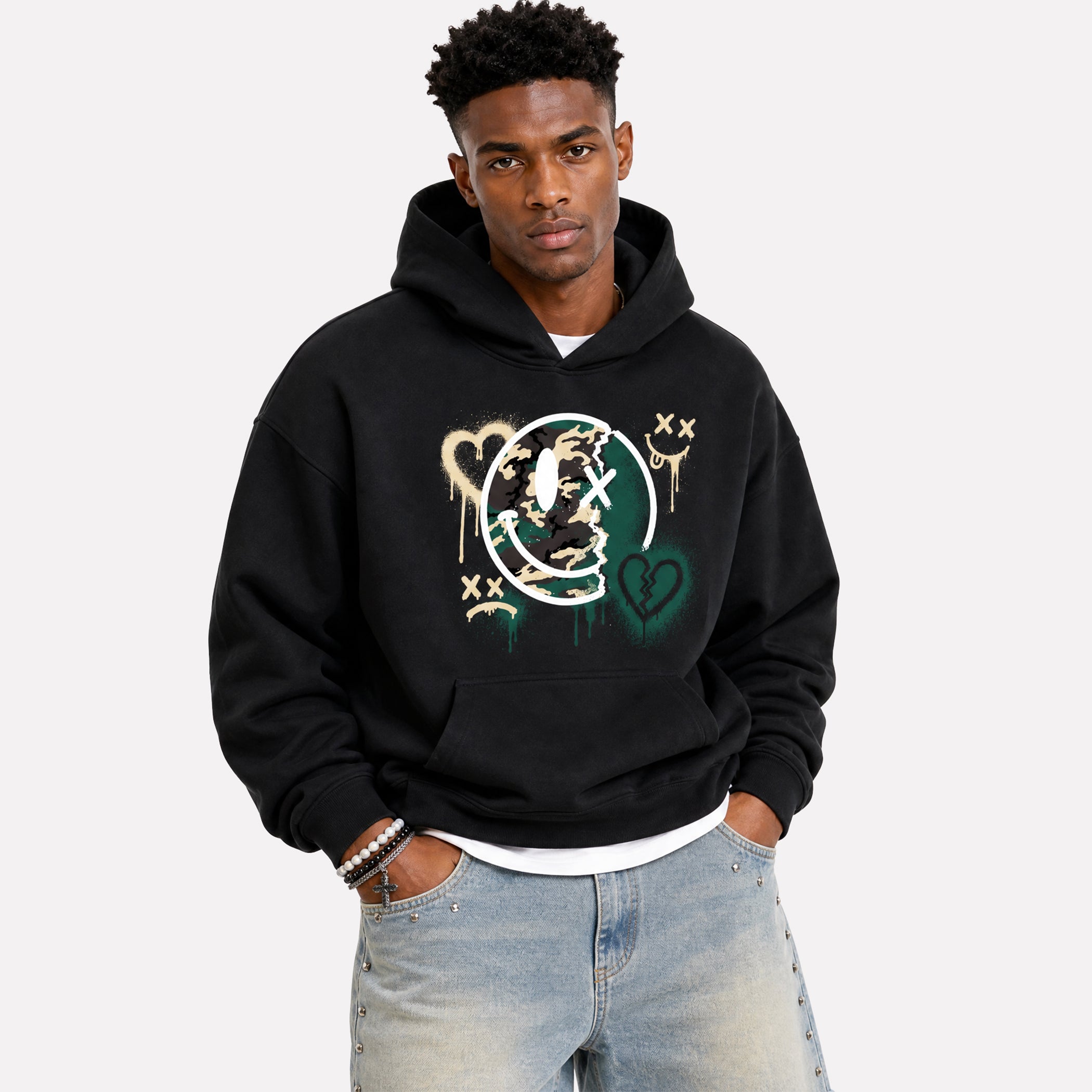 A man wearing a black pullover hoodie with a colorful graffiti-style graphic on the front, paired with light-wash jeans, against a plain light gray background.