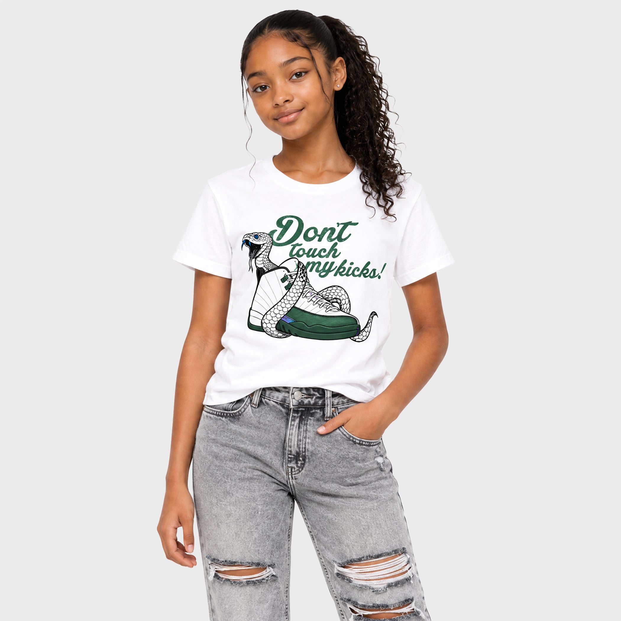 A young woman modeling a white graphic t-shirt with a green snake illustration and the text 'Don't touch my kicks!' paired with distressed gray jeans, set against a solid light gray background.