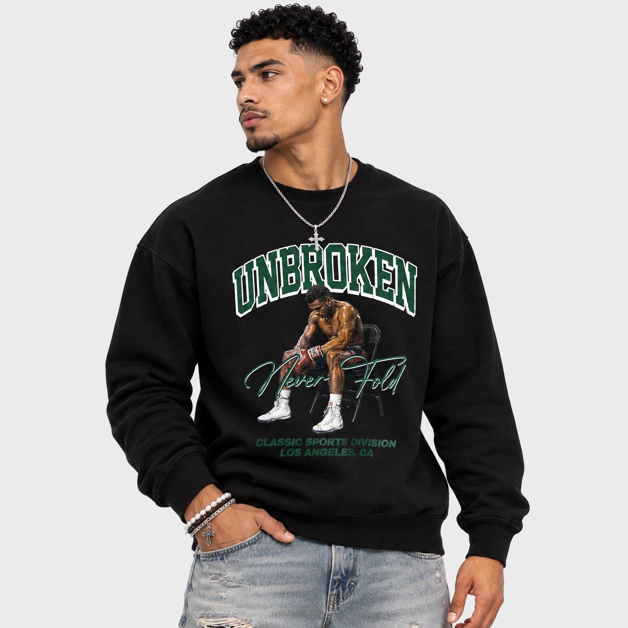 A man wearing a black crewneck sweatshirt with a green and white graphic of a basketball player and the text 'UNBROKEN Never Fold' on a light gray background.