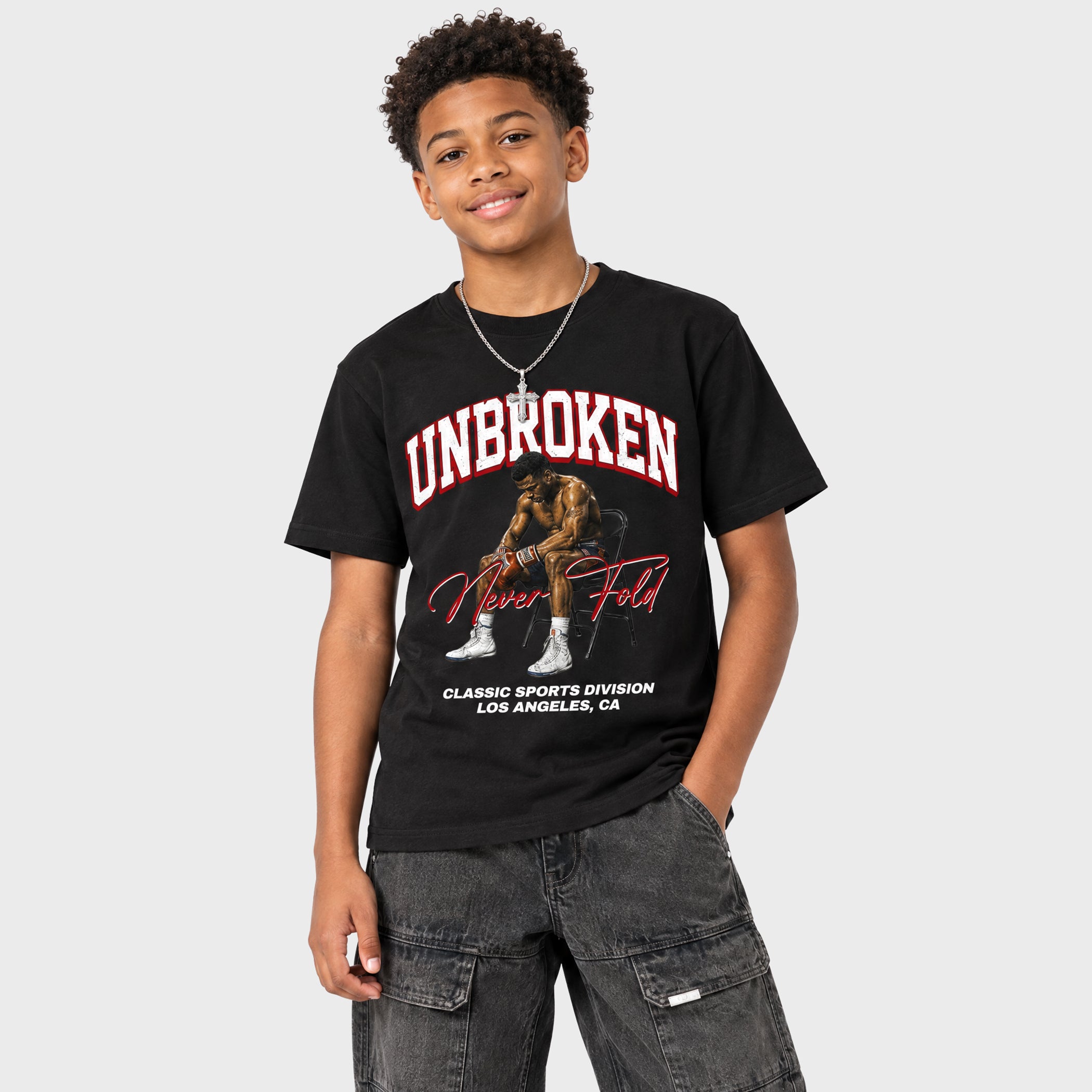 A young man wearing a black graphic t-shirt with 'UNBROKEN Never Fold' and a sports-themed illustration, paired with gray cargo pants, against a light gray background.